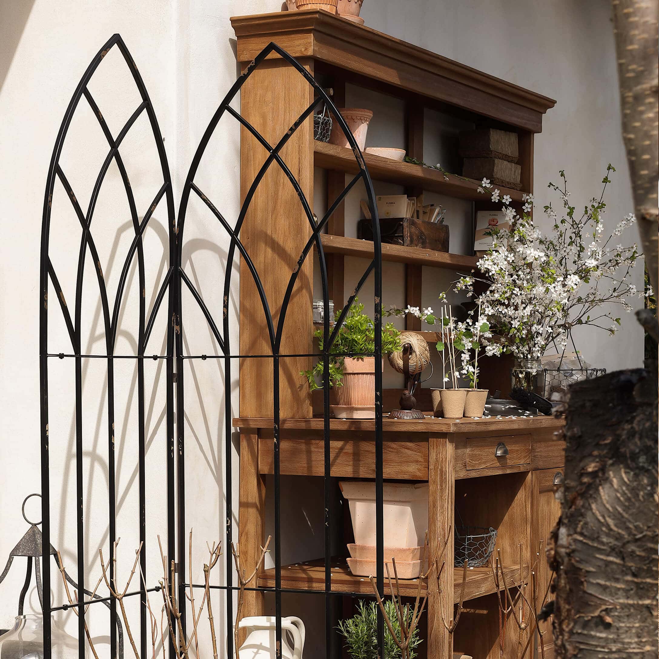 Griglia da giardino in metallo nero con motivo ad arco davanti a scaffale in legno con vasi e fiori