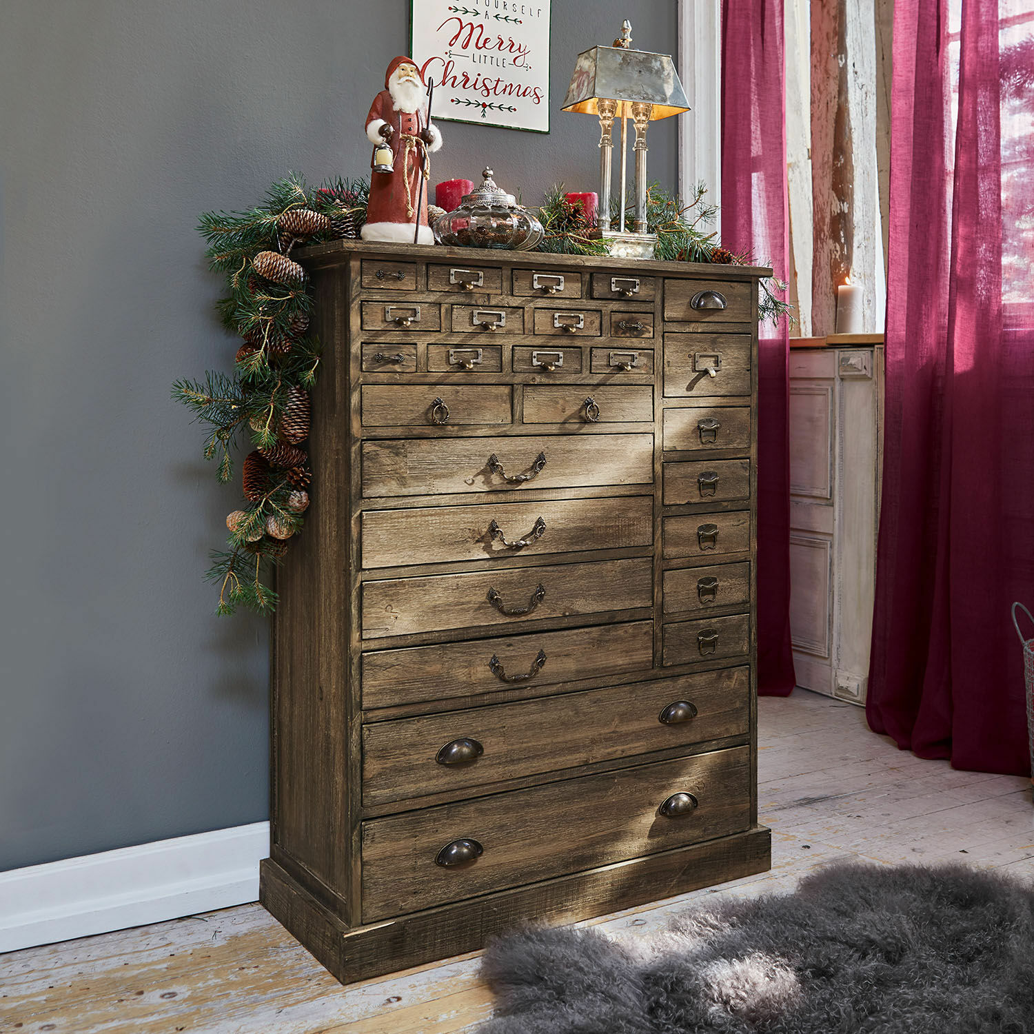 Cassettiera in legno vintage con molti cassetti, decorata con addobbi natalizi e lampada argento
