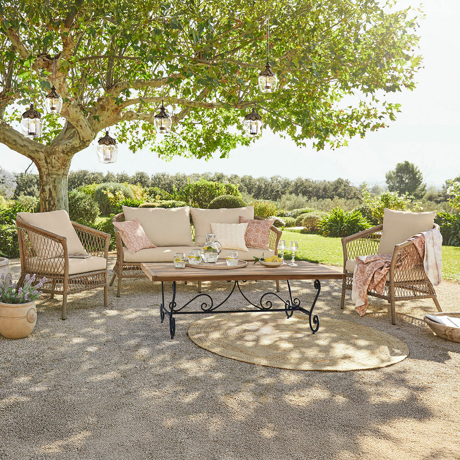 Salottino Farington Set di mobili da giardino in rattan con cuscini beige e tavolo in legno su terrazza soleggiata