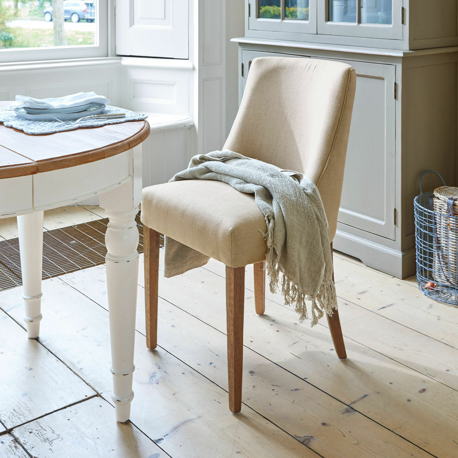 Sedia Opirel Sedia imbottita beige con gambe in legno e coperta grigia in sala da pranzo luminosa