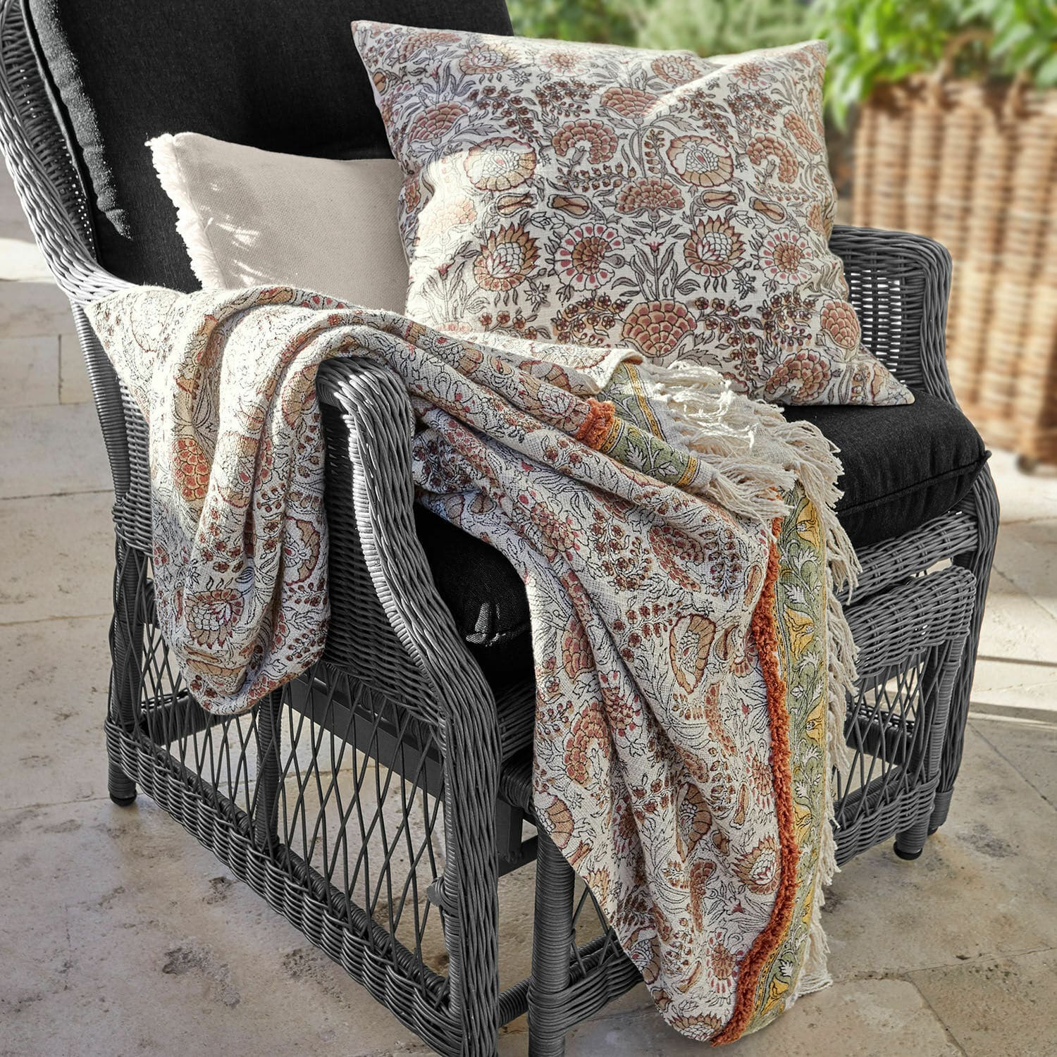 Plaid Romila Coperta e cuscino in cotone con motivo floreale caldo su poltrona grigia in rattan per decorazione