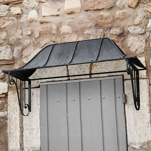 Pensilina in metallo nero sopra porta grigia su muro in pietra, elemento decorativo esterno