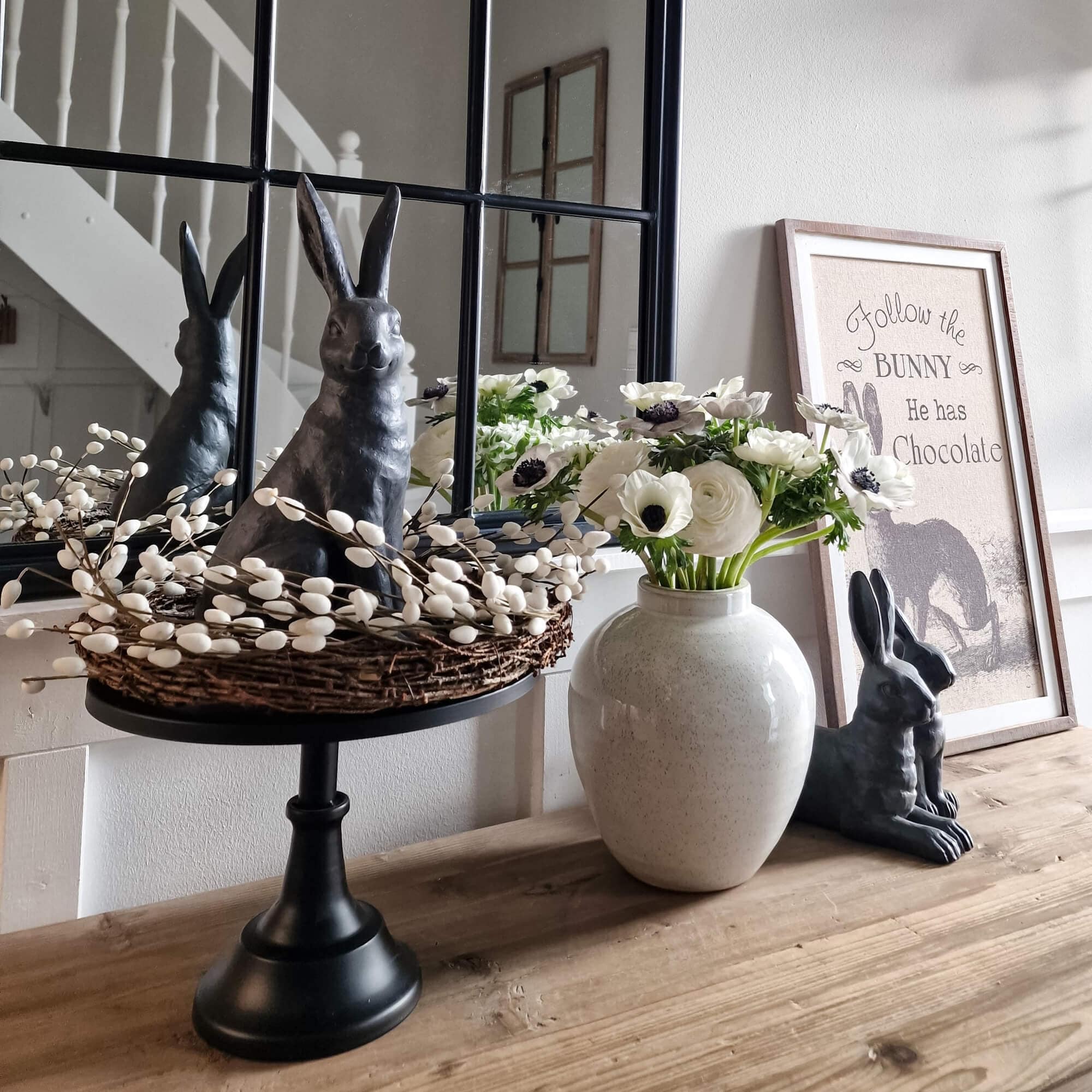 Coniglio decorativo nero con corona di vimini e fiori bianchi in vaso di ceramica su tavolo in legno