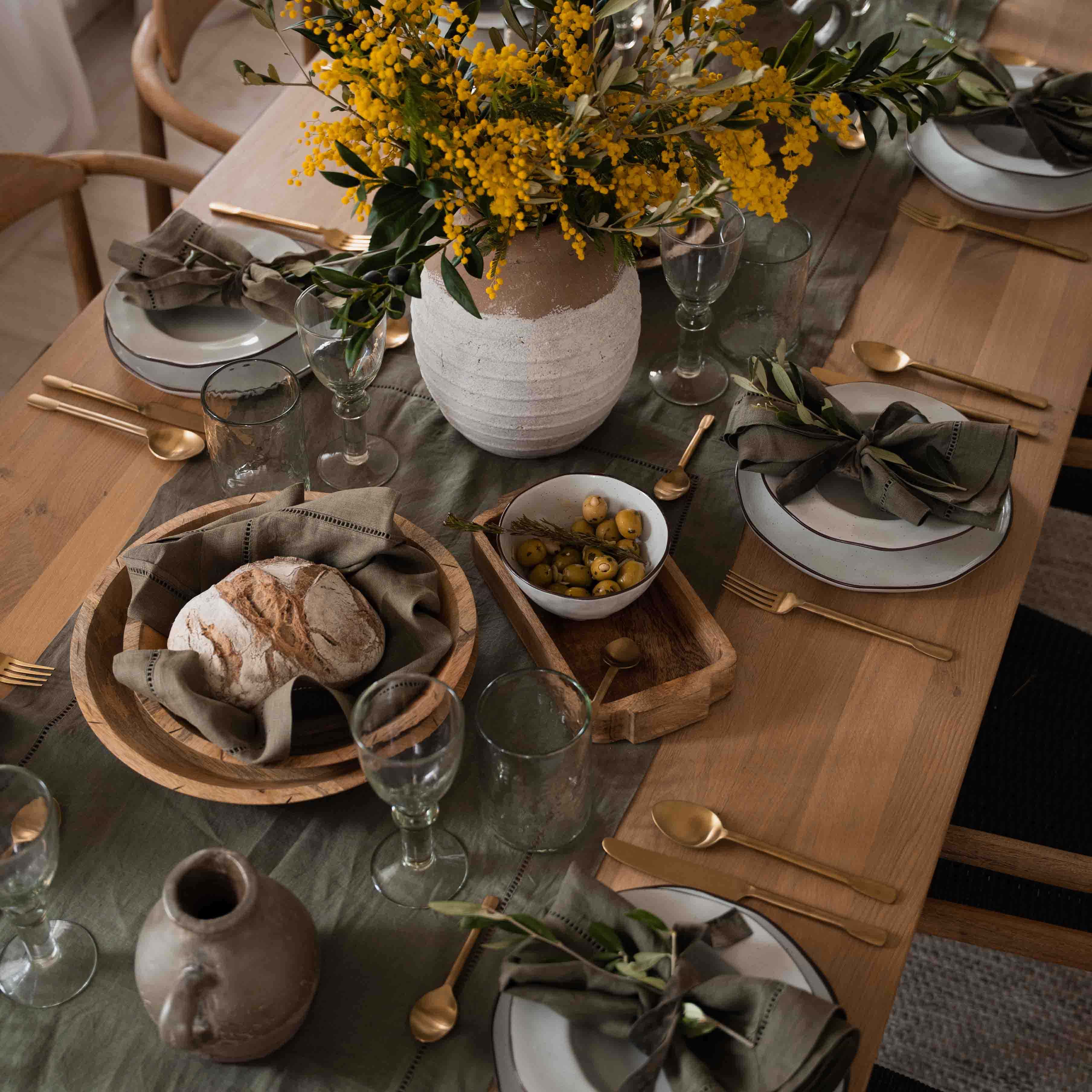 Tavolo rustico in legno con stoviglie bianche, tovaglioli verdi e mazzo di fiori gialli in vaso di terracotta