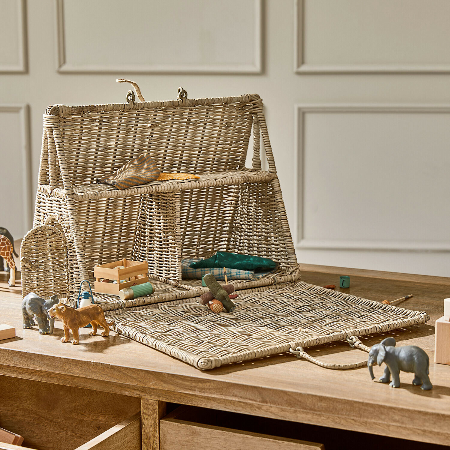 Casetta per bambole in vimini naturale con fronte apribile e giocattoli in legno sul tavolo