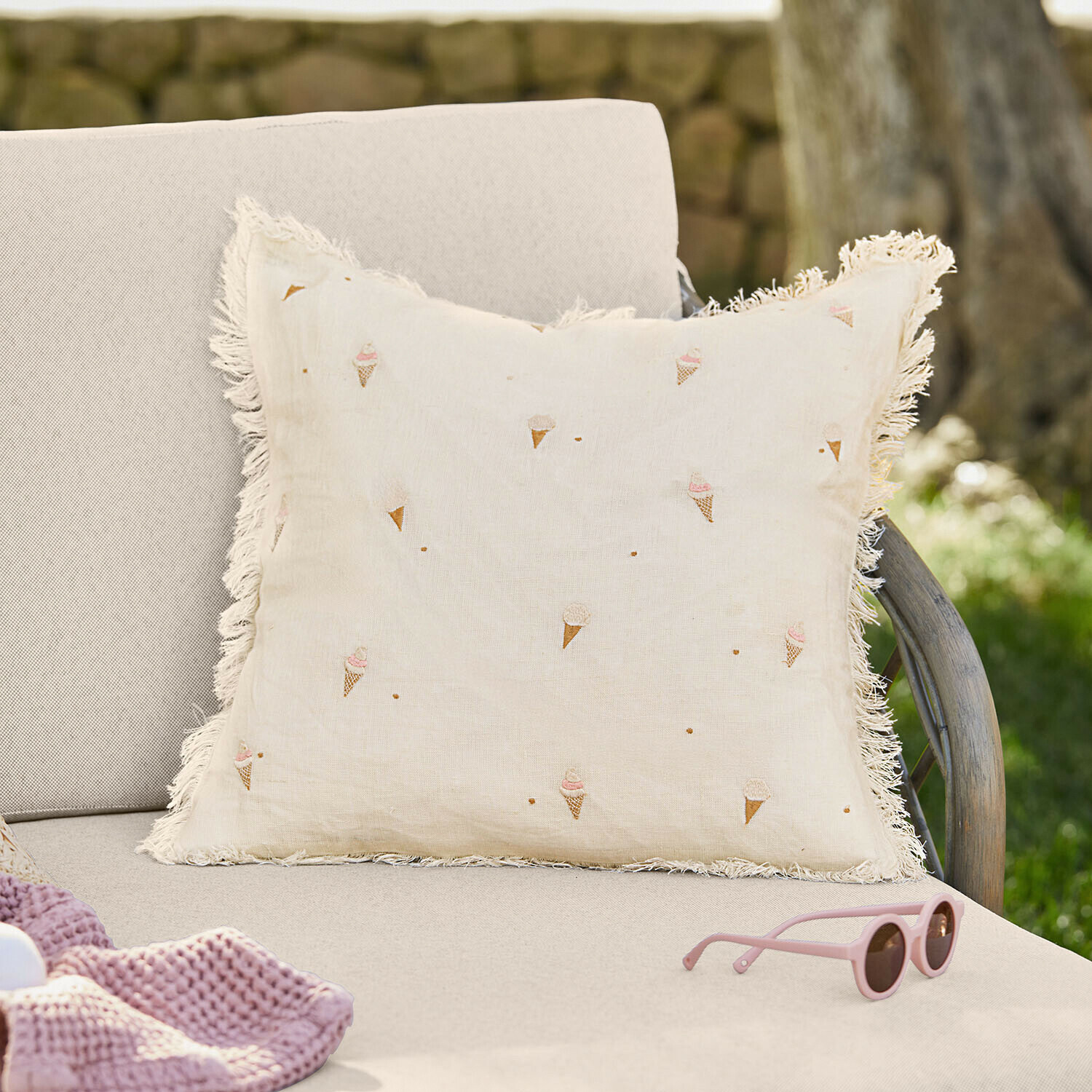 Copricuscino Toffelis Cuscino beige in lino con frange e motivo con coni gelato su divano chiaro in giardino