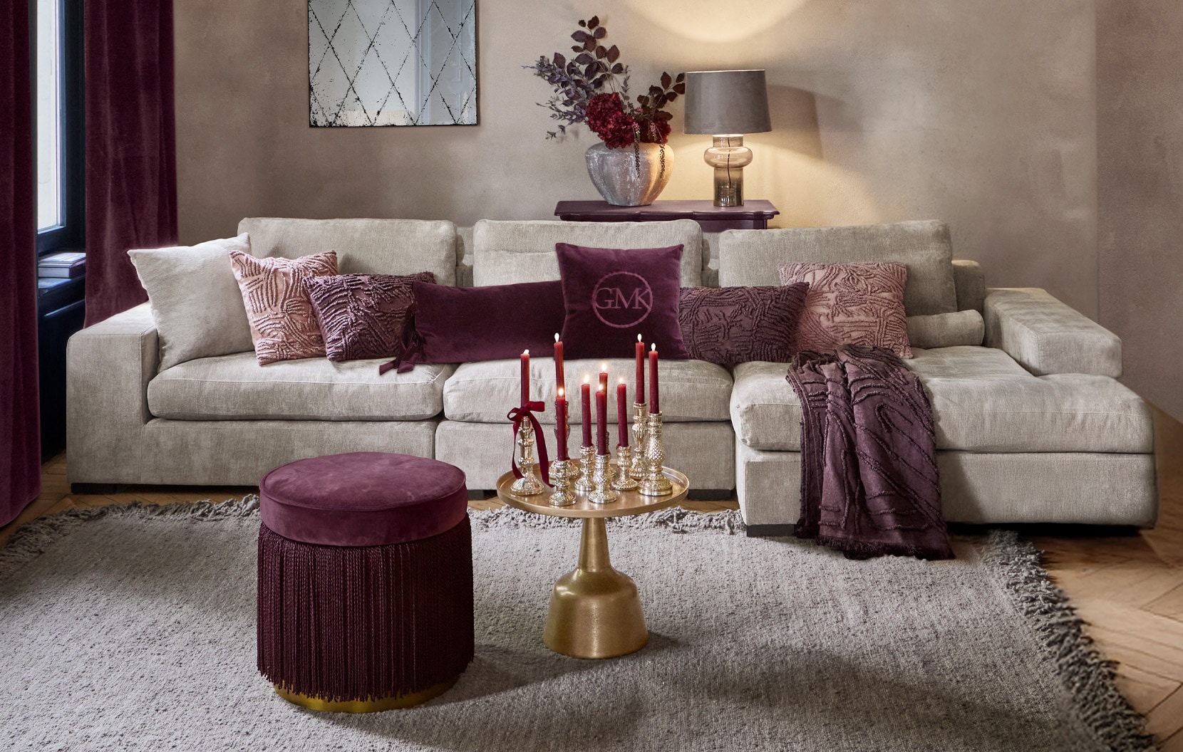 Divano beige con cuscini viola e pouf bordeaux in soggiorno elegante con candele decorative