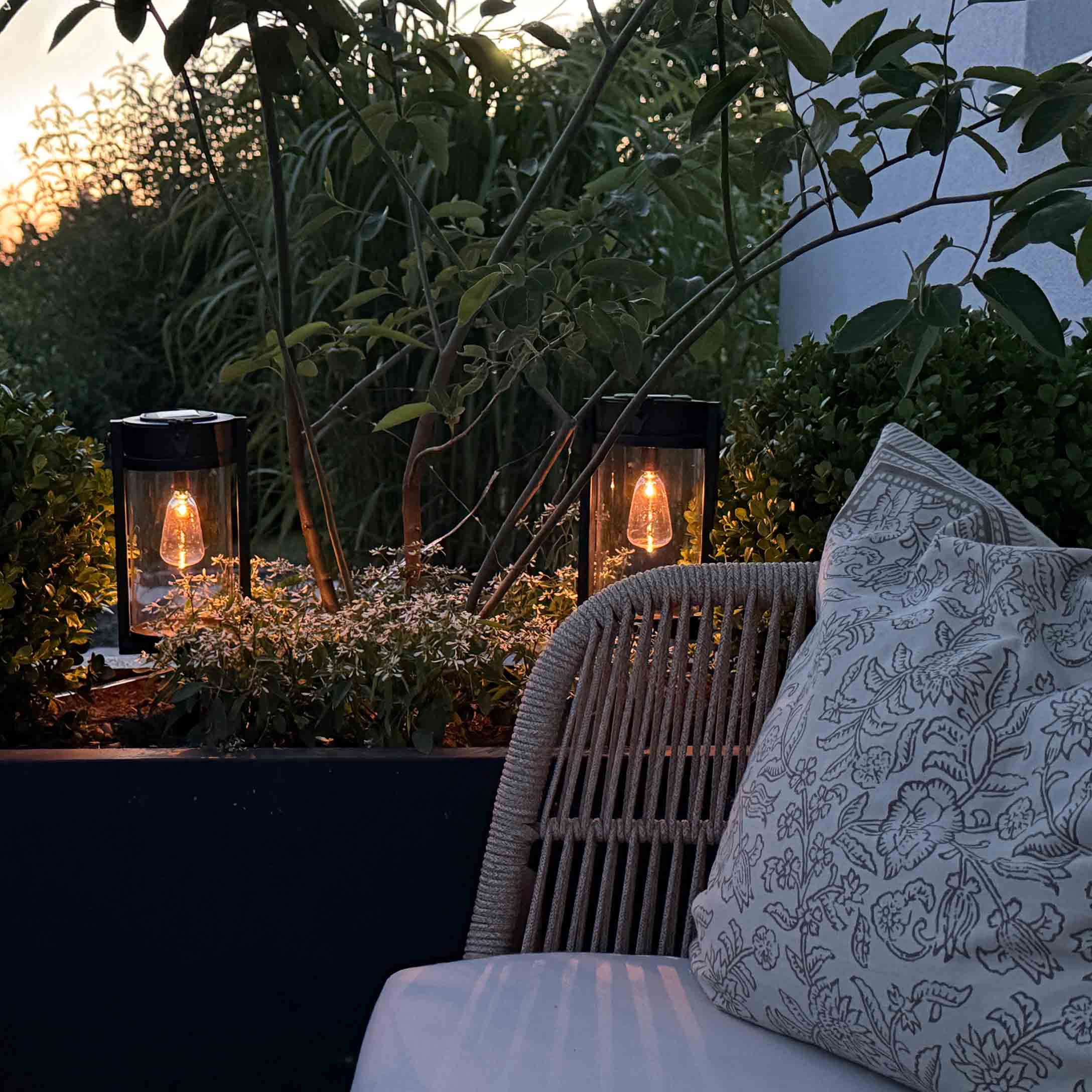 Lanternes da giardino in metallo nero con luce calda tra piante verdi sulla terrazza