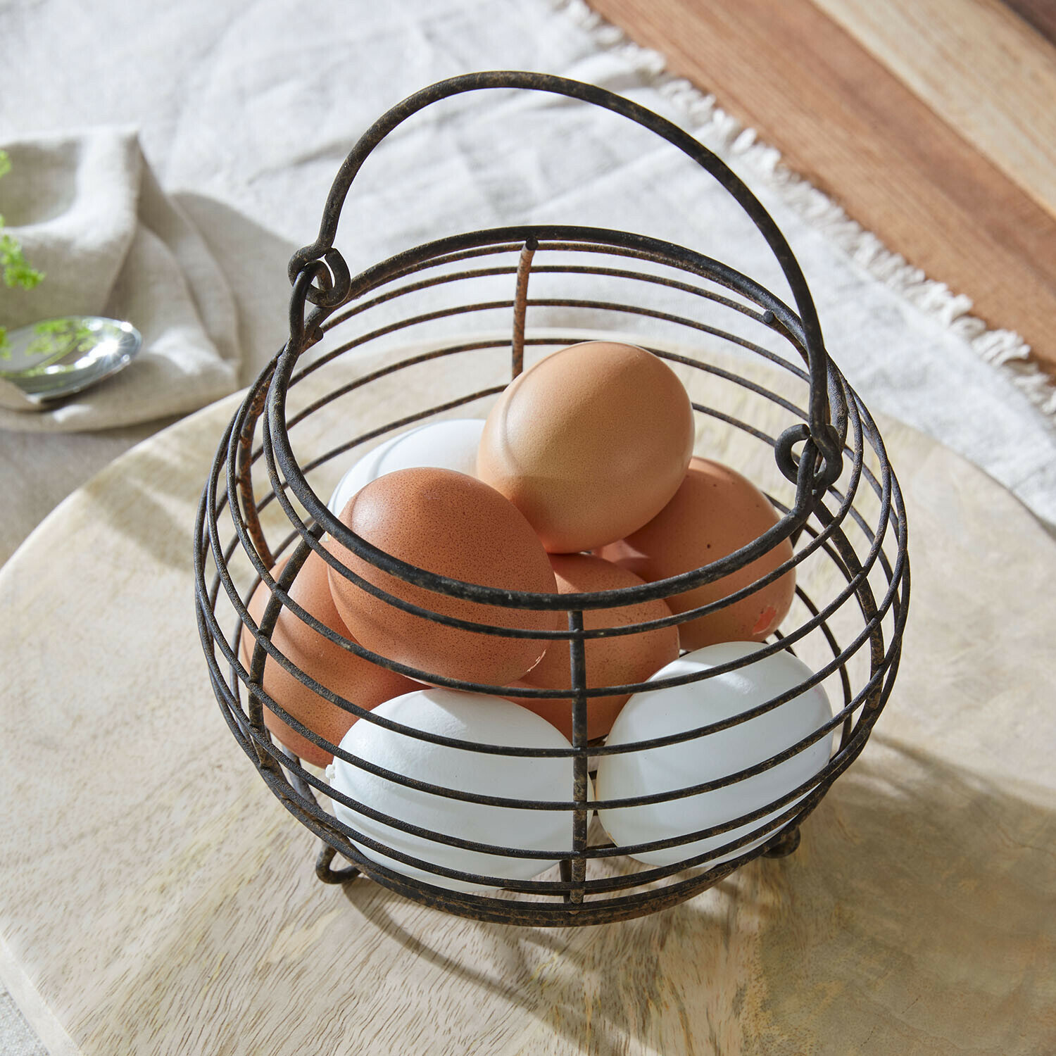Cestino vintage in metallo per uova con uova marroni e bianche su superficie in legno chiaro