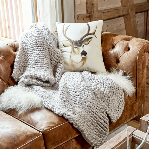 Coperta spessa grigia in lana su divano in pelle marrone con cuscino decorativo cervo