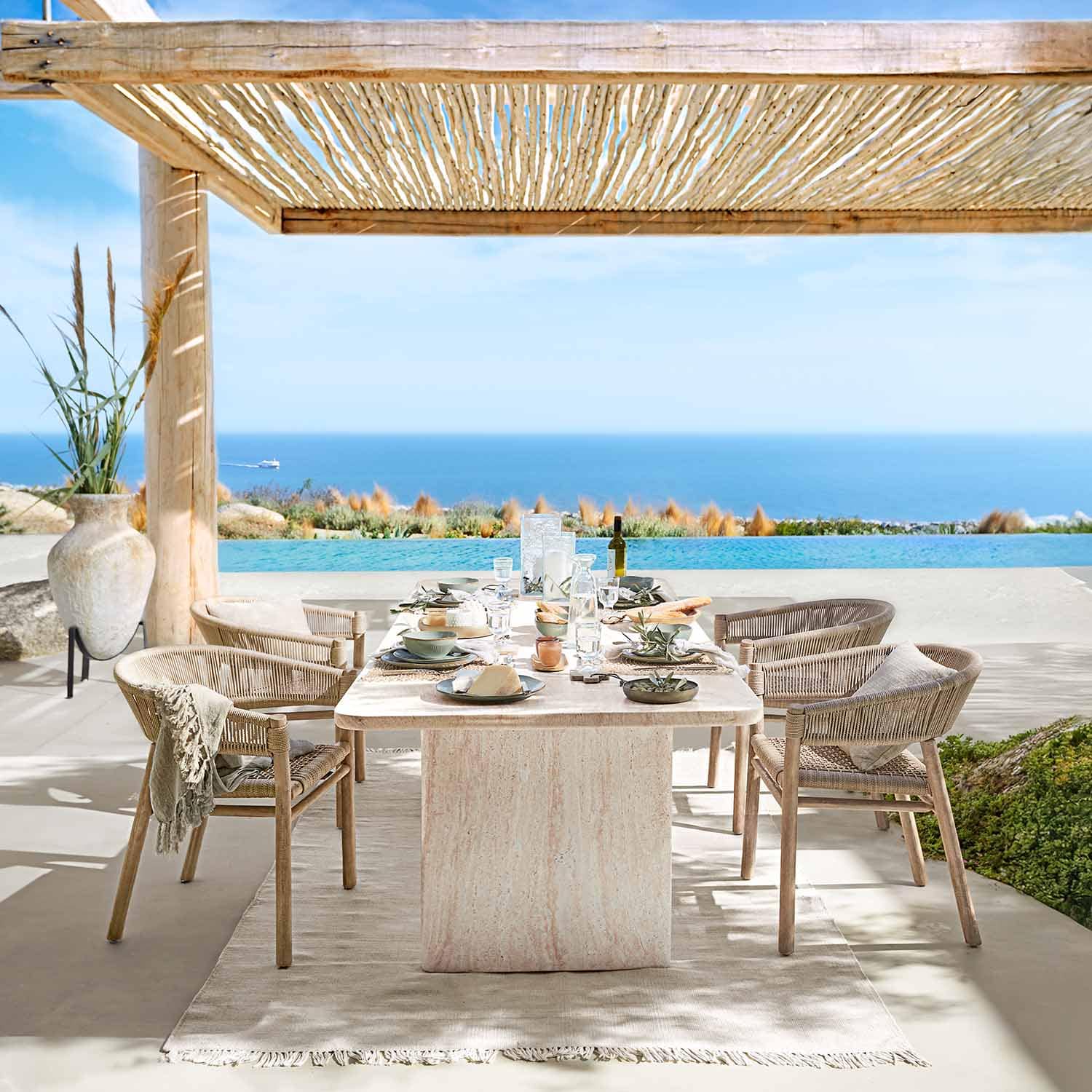 Zona pranzo esterna con tavolo in pietra naturale e sedie in vimini con vista mare