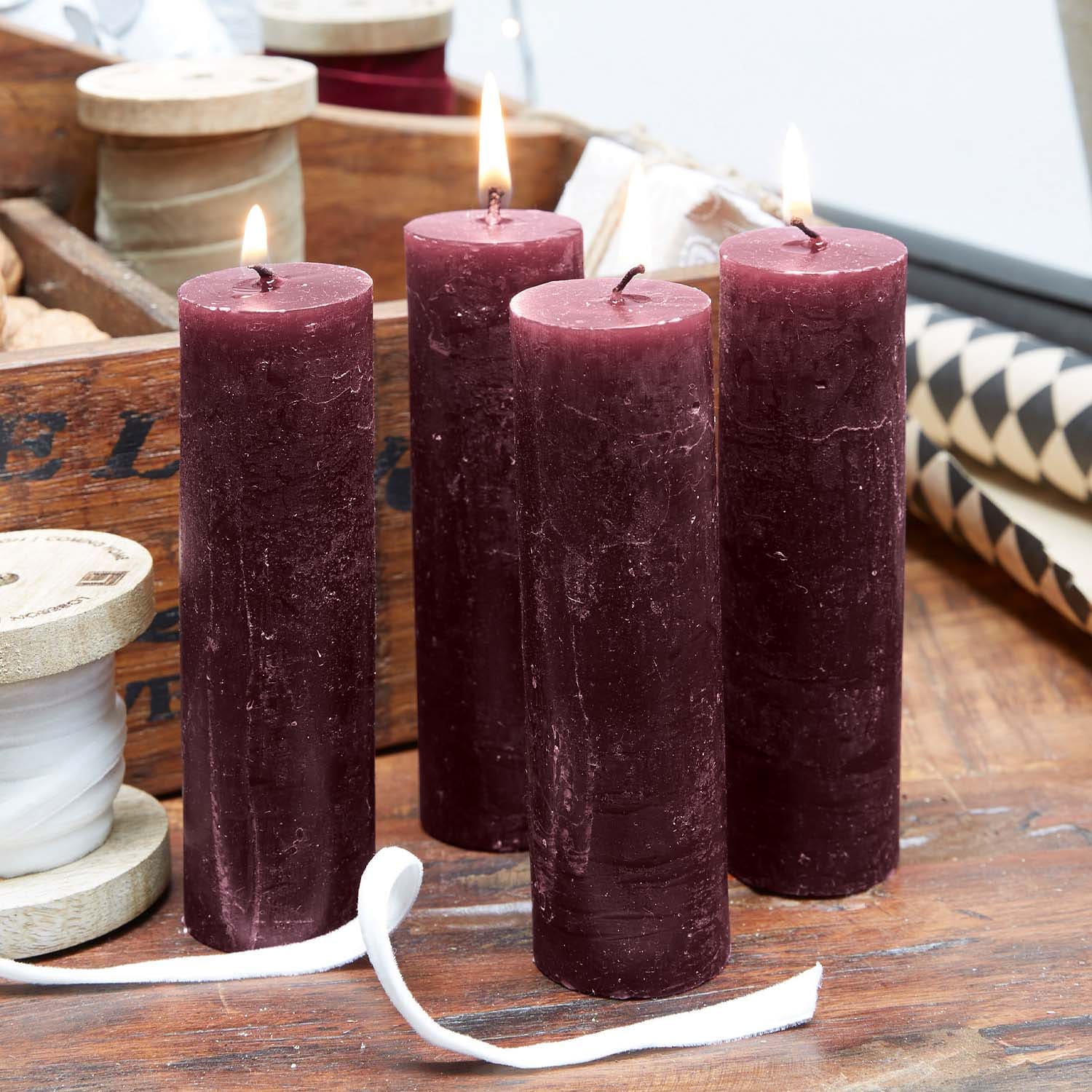 Quattro candele cilindriche color bordeaux in cera su tavolo di legno, decorazione accogliente