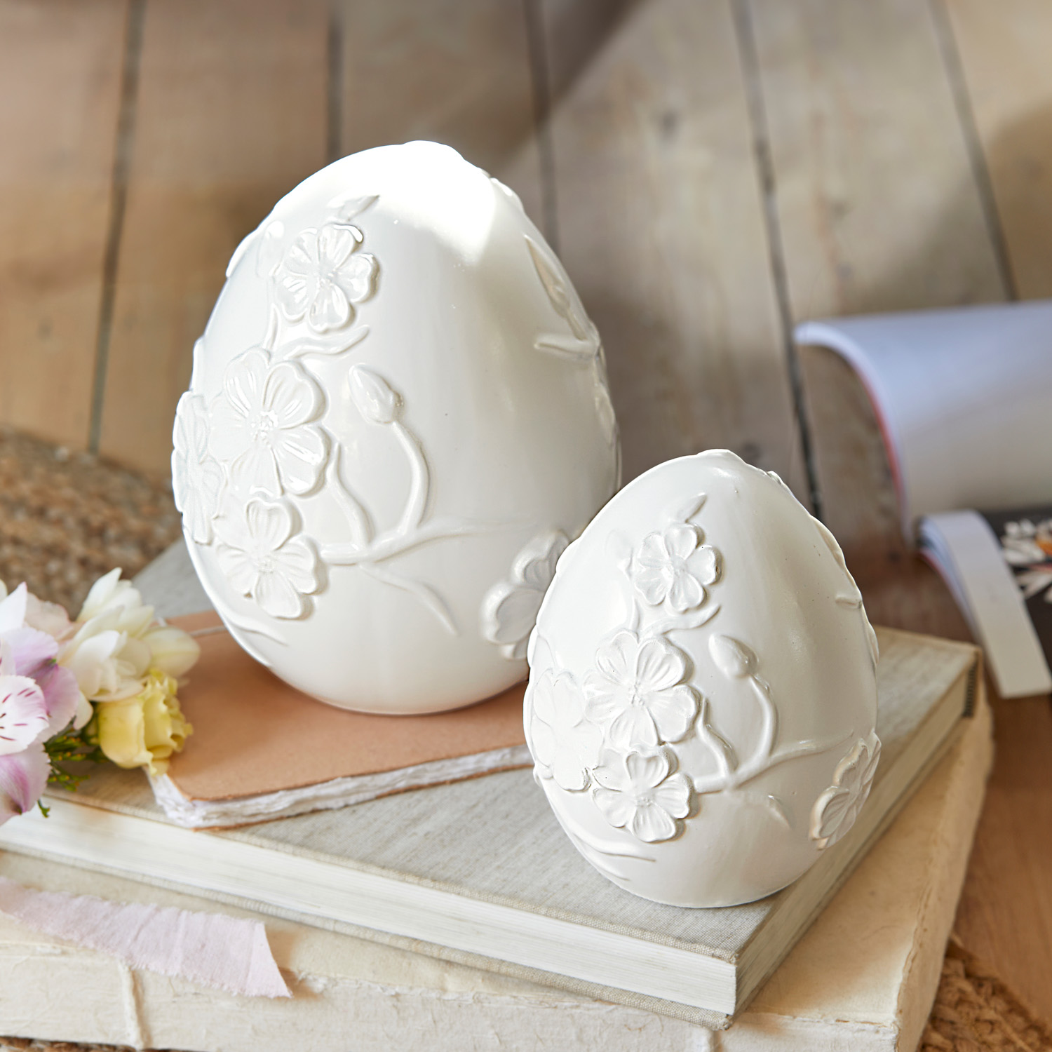 Uova decorative in ceramica bianca con rilievo floreale su libri, decorazione primaverile