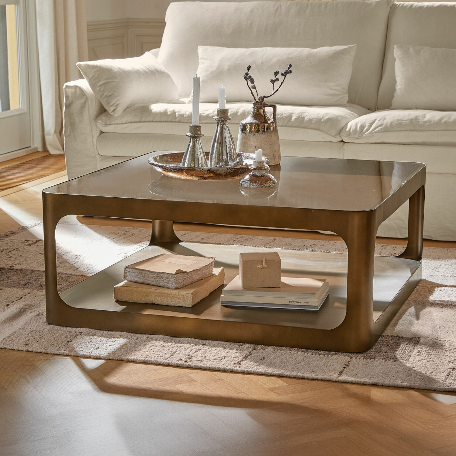 Tavolino da salotto Bexington Tavolino quadrato in metallo color ottone con ripiano e decorazioni su tappeto chiaro