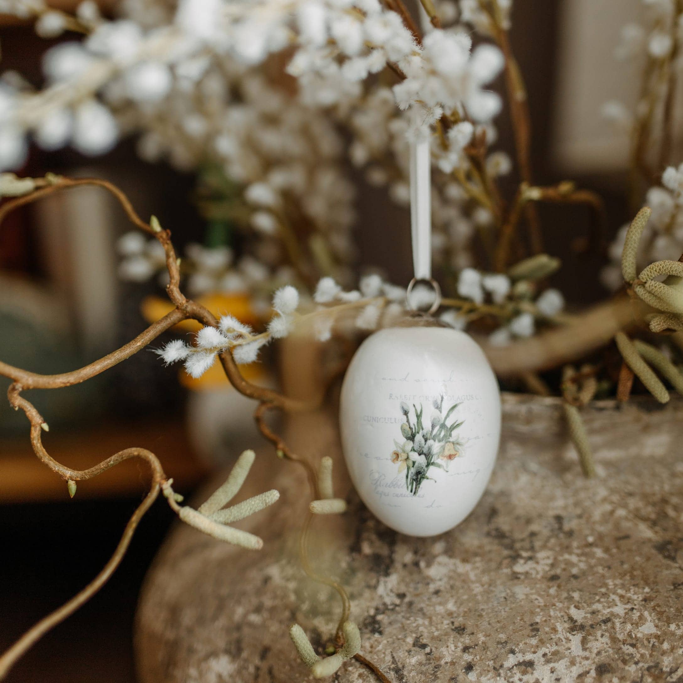 Decorazione pasquale in ceramica bianca a forma di uovo con motivo floreale appesa a un ramo decorativo