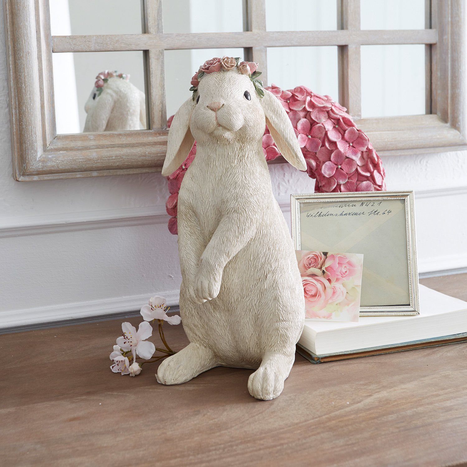 Lepre Sweety Figura di coniglio in materiale color crema con corona di fiori rosa su tavolo decorato