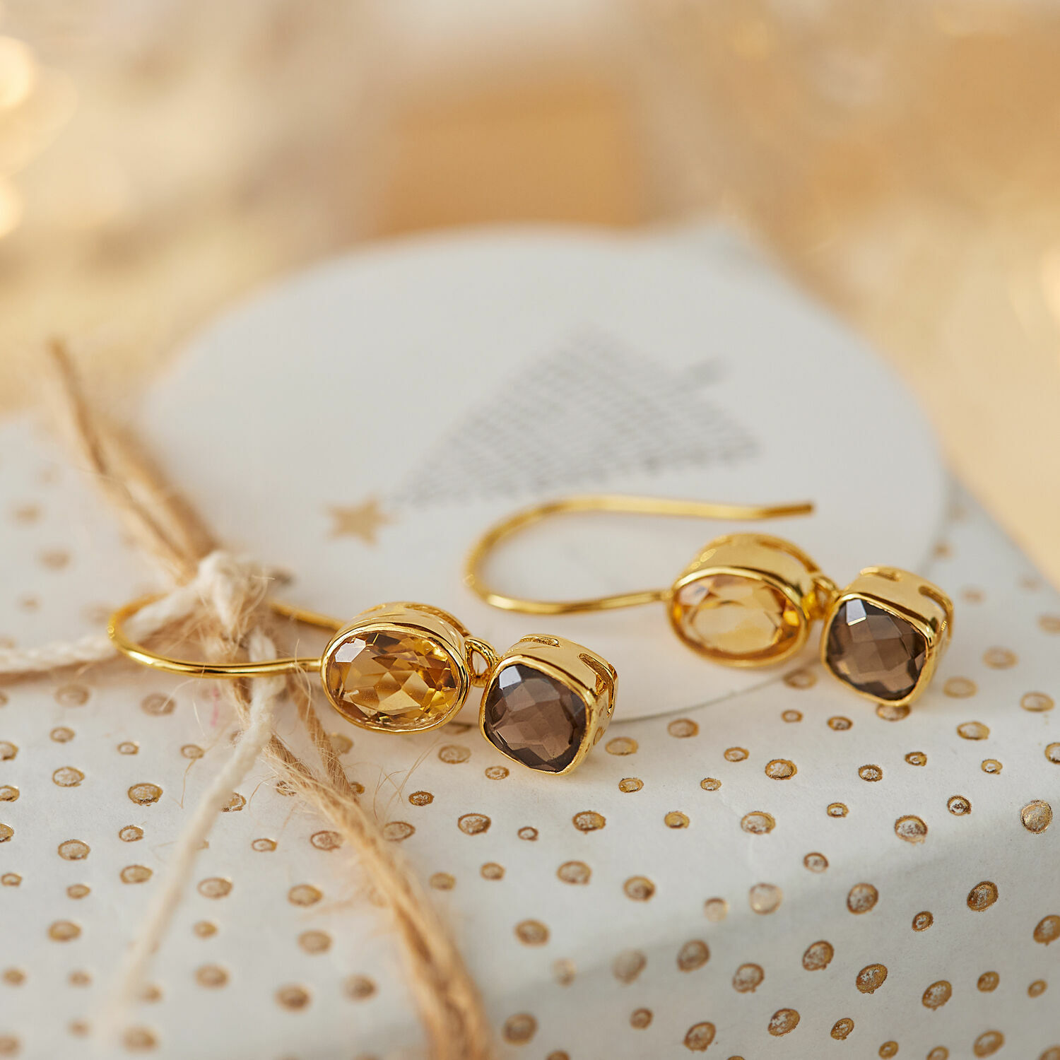 Orecchini Ovique Orecchini dorati con pietre sfaccettate marroni su carta regalo decorativa