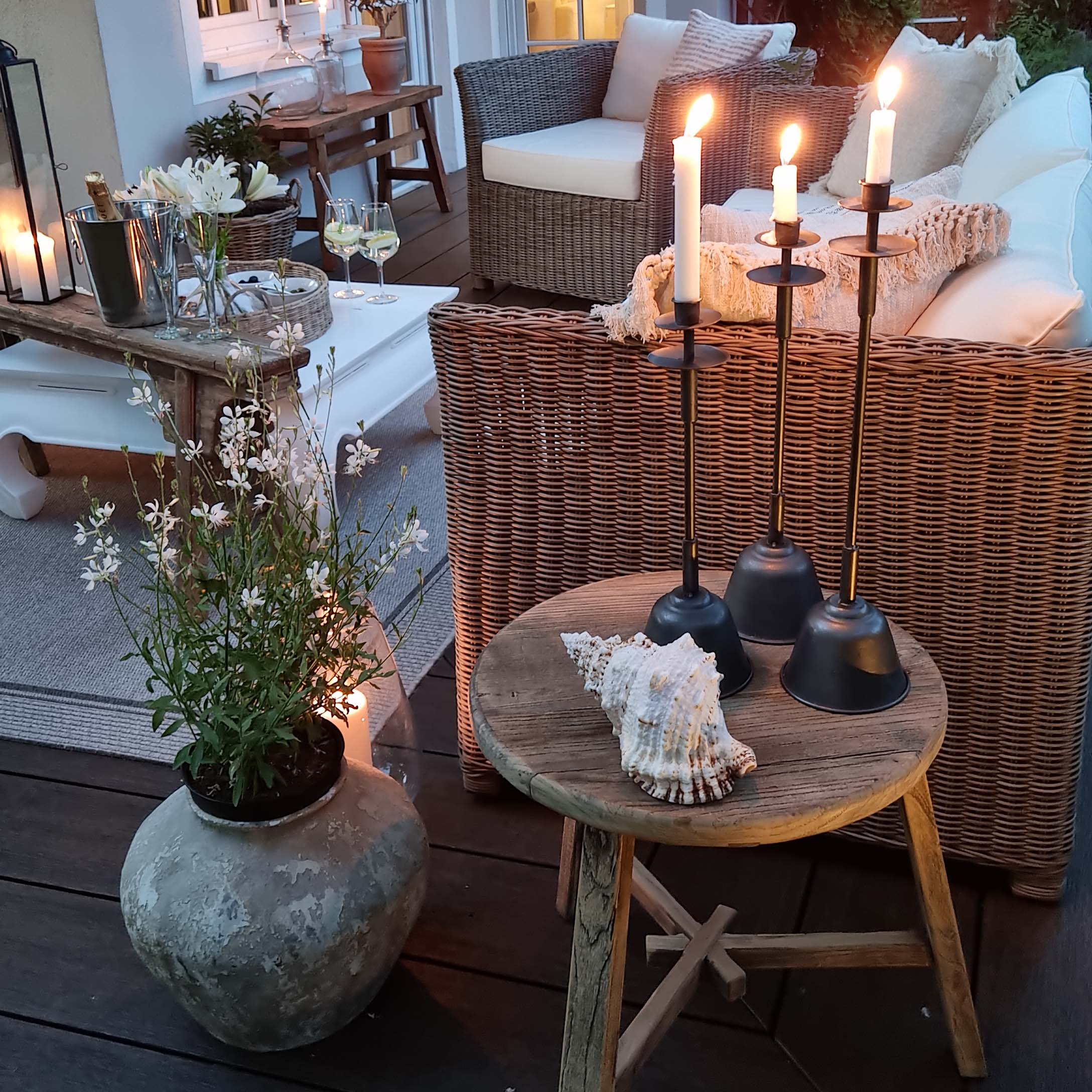 Accogliente terrazza con divano in rattan, tavolino in legno e candelabri in metallo con candele bianche