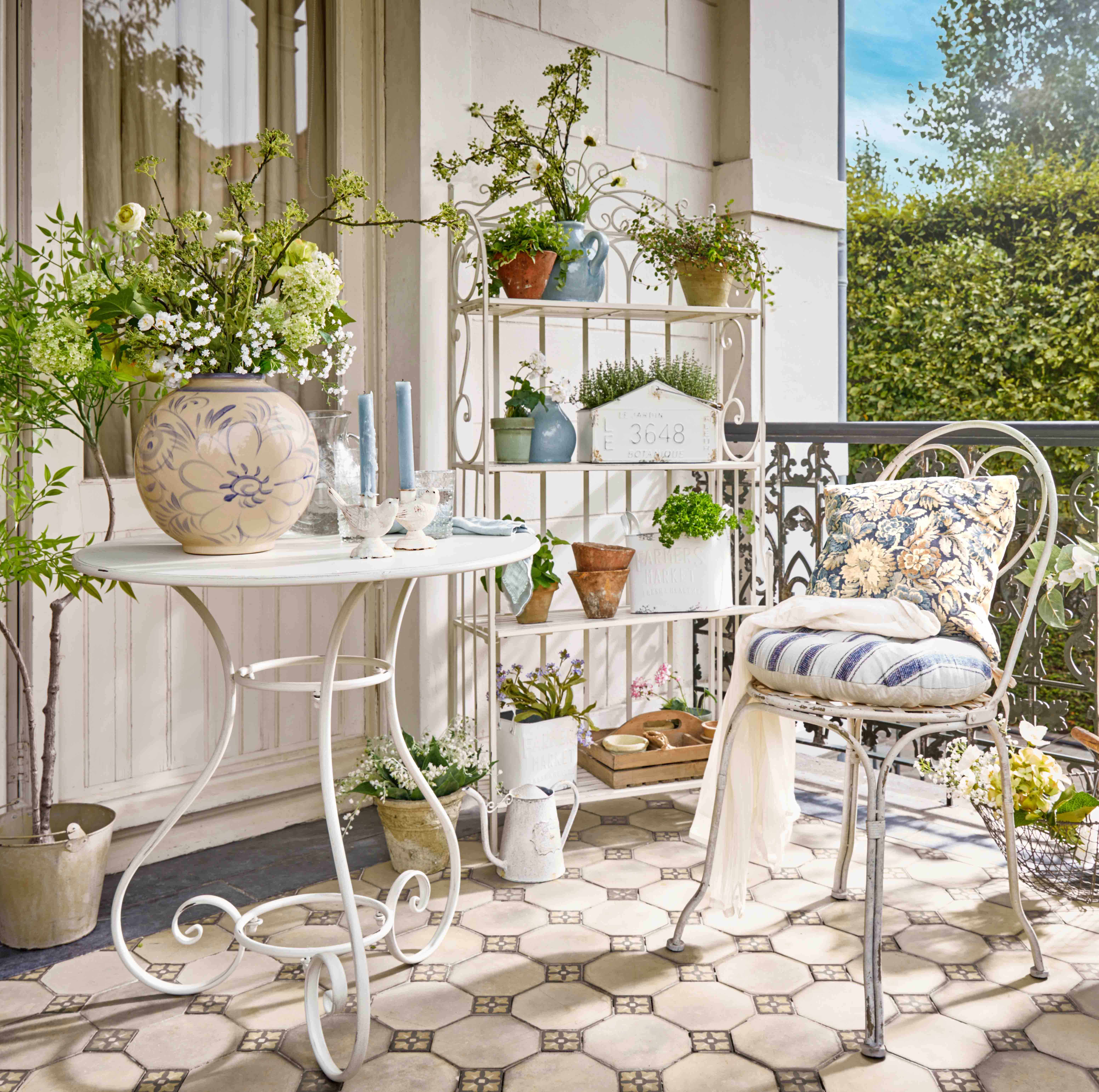 Scaffale in metallo bianco con piante in vaso e candele decorative su terrazza fiorita