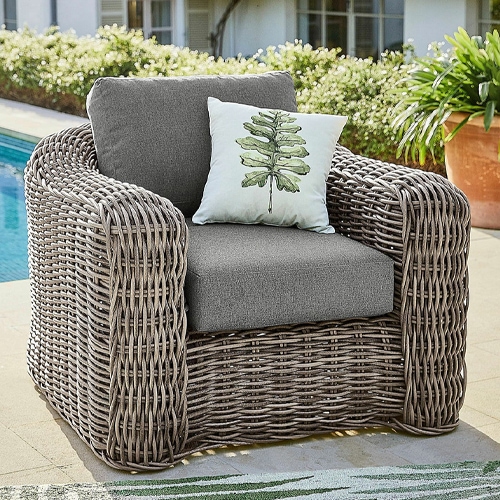 Poltrona da giardino in vimini grigio con cuscini grigi e cuscino decorativo con foglia verde