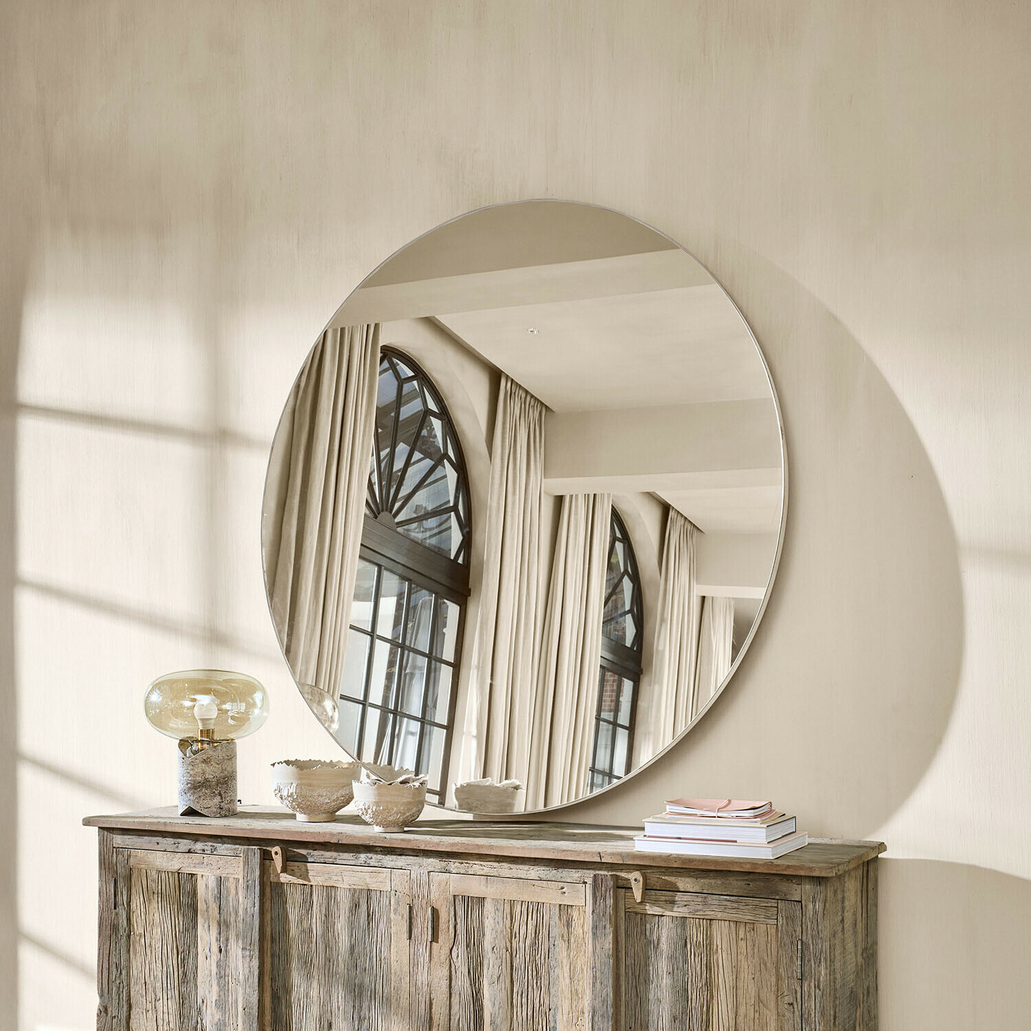 Grande specchio rotondo appeso sopra una credenza in legno in un interno luminoso e naturale