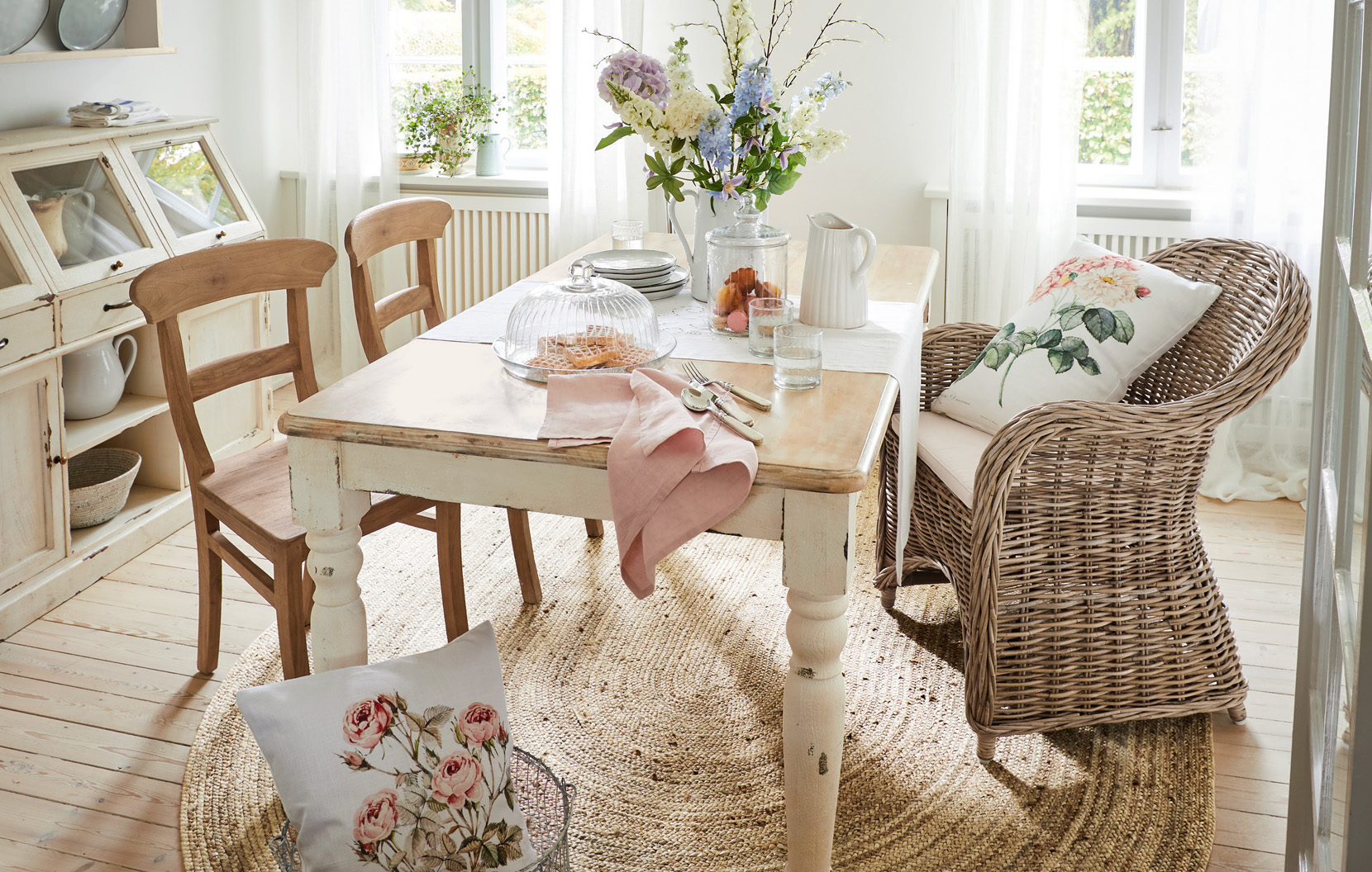 Sala da pranzo shabby chic con tavolo in legno, poltrona in vimini e decorazioni floreali