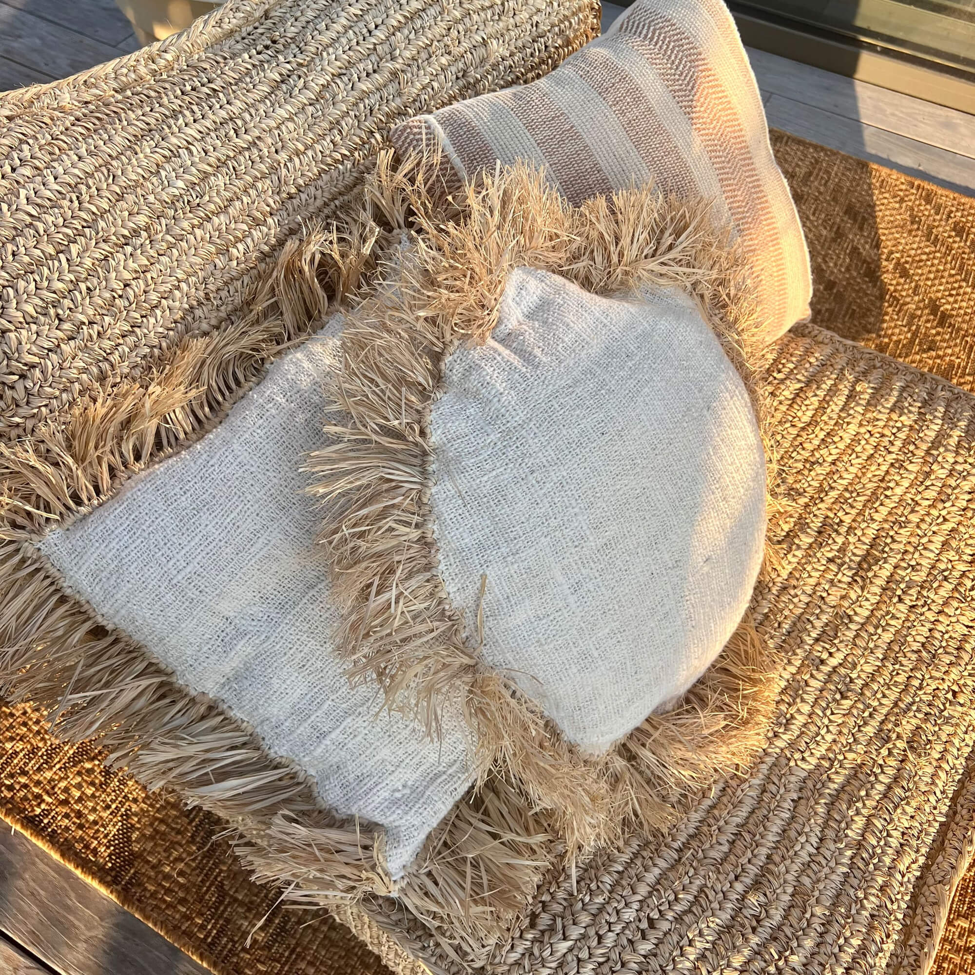 Cuscini decorativi in materiali naturali beige su poltrona intrecciata da giardino