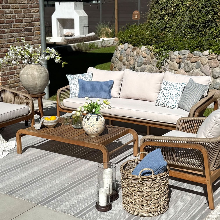 Set di mobili da giardino in legno con divano beige e cuscini blu a motivi su tappeto a righe