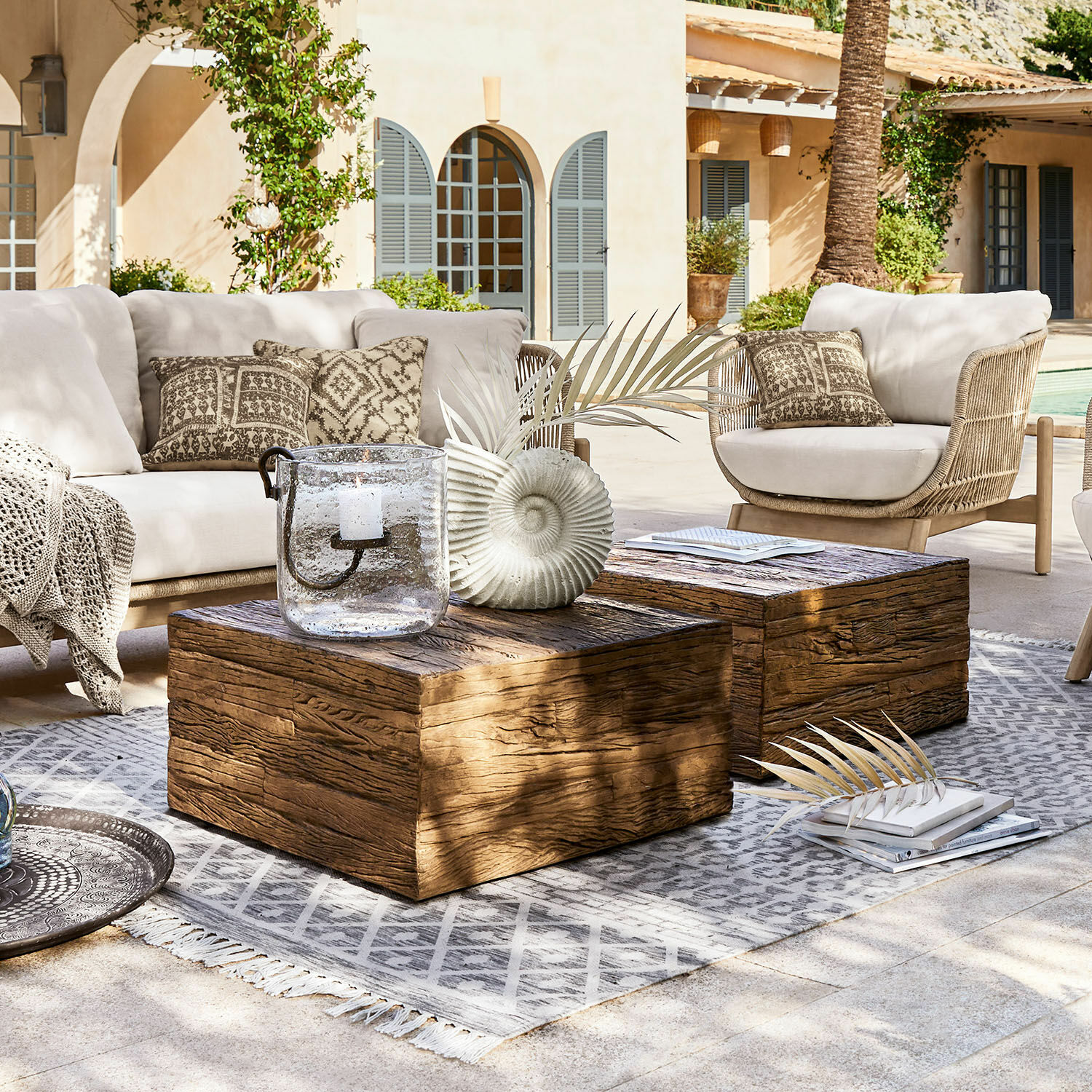 Tavolino da salotto Glâne Set di mobili da giardino con cuscini chiari e tavolini in legno su tappeto grigio in terrazza