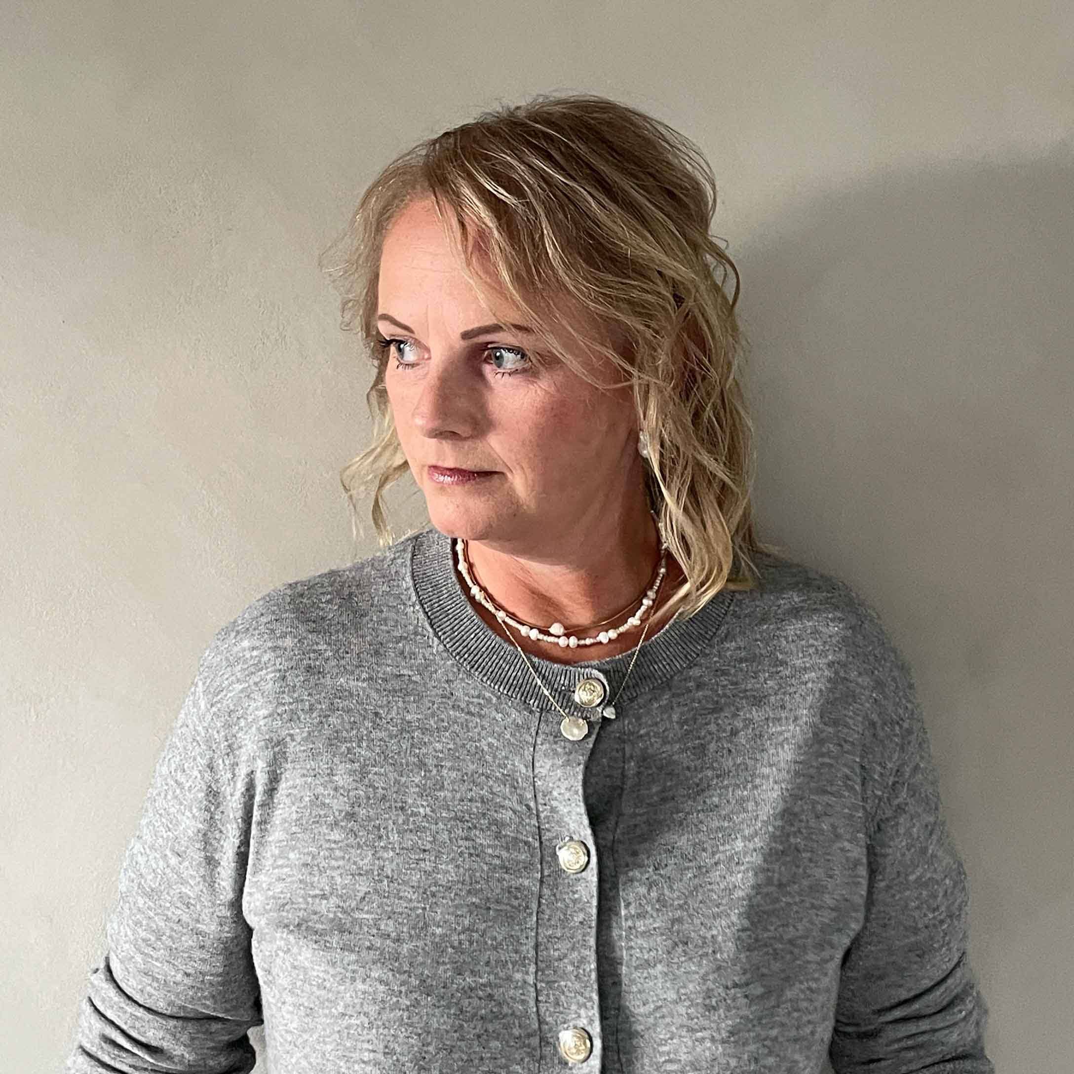Donna con cardigan grigio con bottoni e collane, stile casual su sfondo chiaro