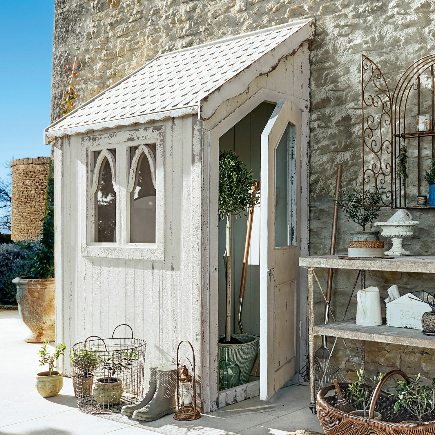 Casetta da giardino Lettret Casetta da giardino in legno bianco con finestre e porta aperta, piante e attrezzi decorativi
