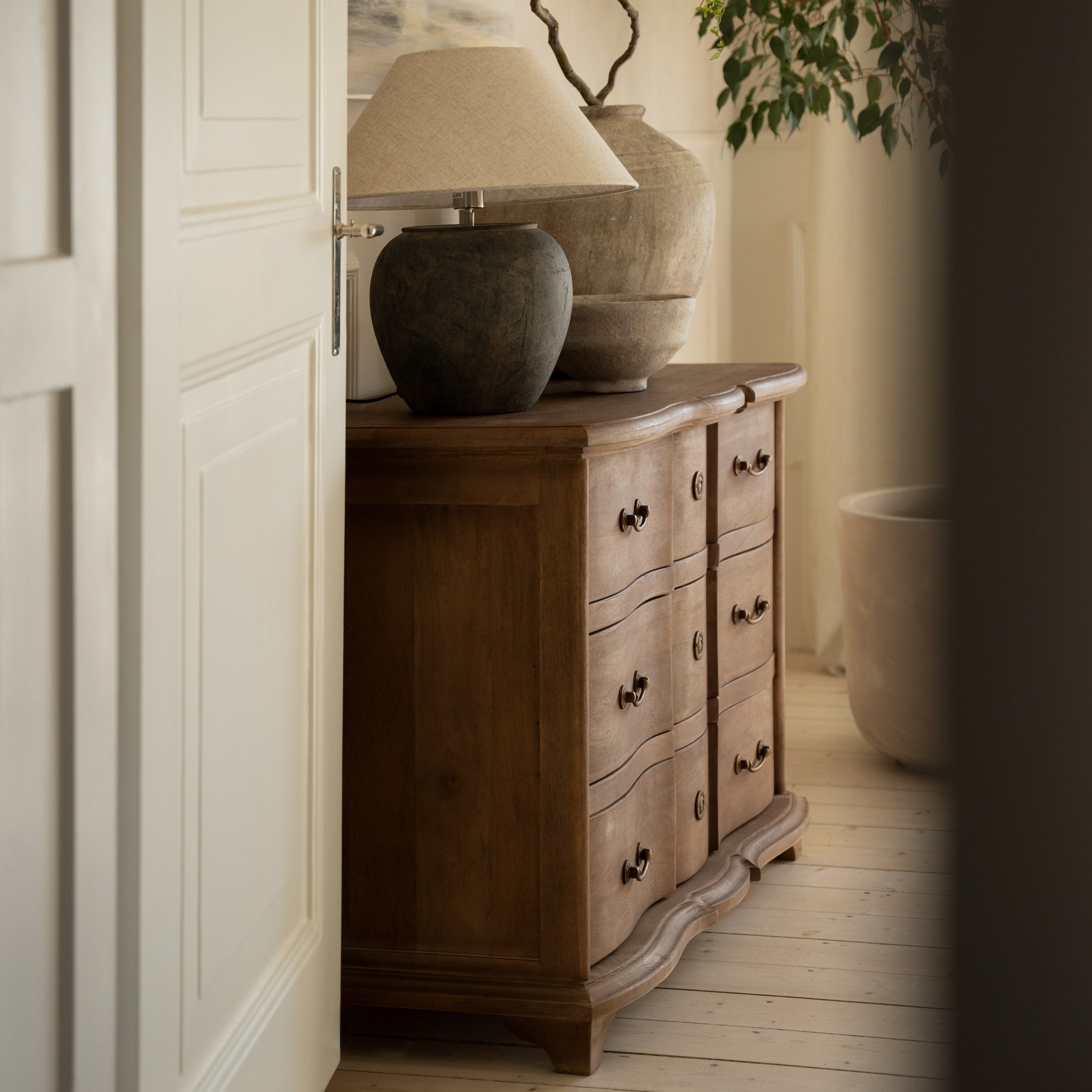 Comò in legno con cassetti decorativi e lampada con paralume beige in ambiente accogliente