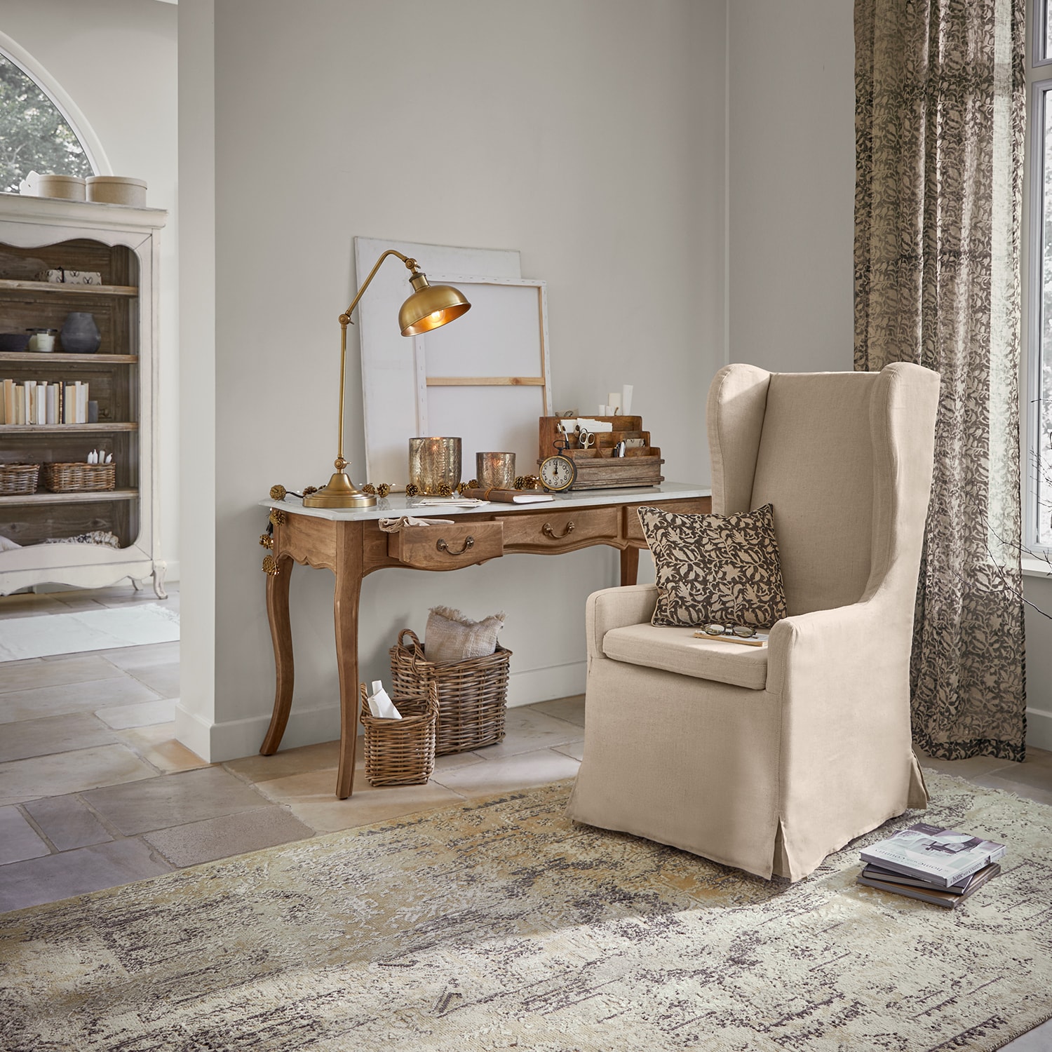 Poltrona beige in tessuto stile orecchioni in soggiorno classico con scrivania in legno e lampada da tavolo