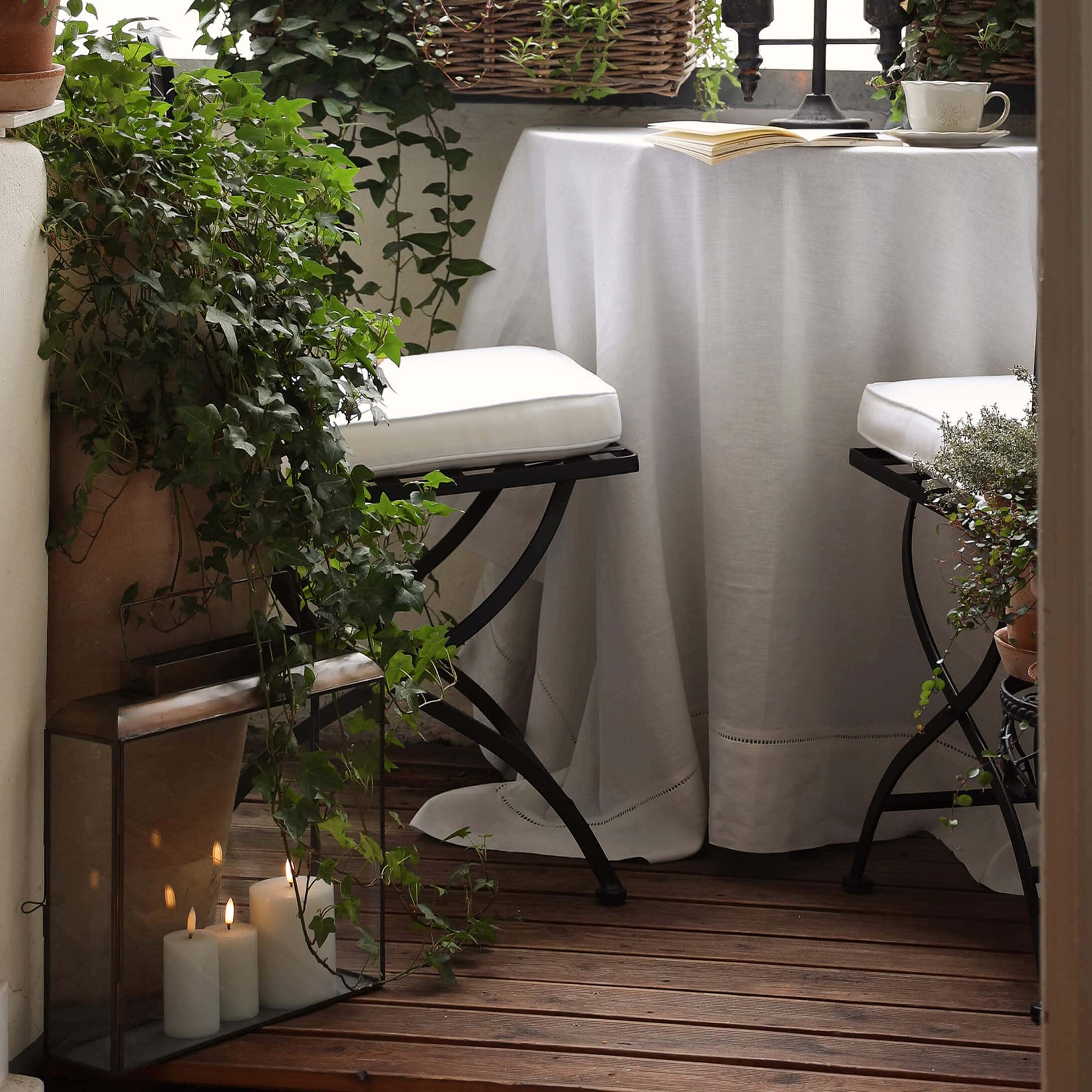 Accogliente balcone con pavimento in legno, tovaglia bianca e sedie in metallo con cuscini bianchi