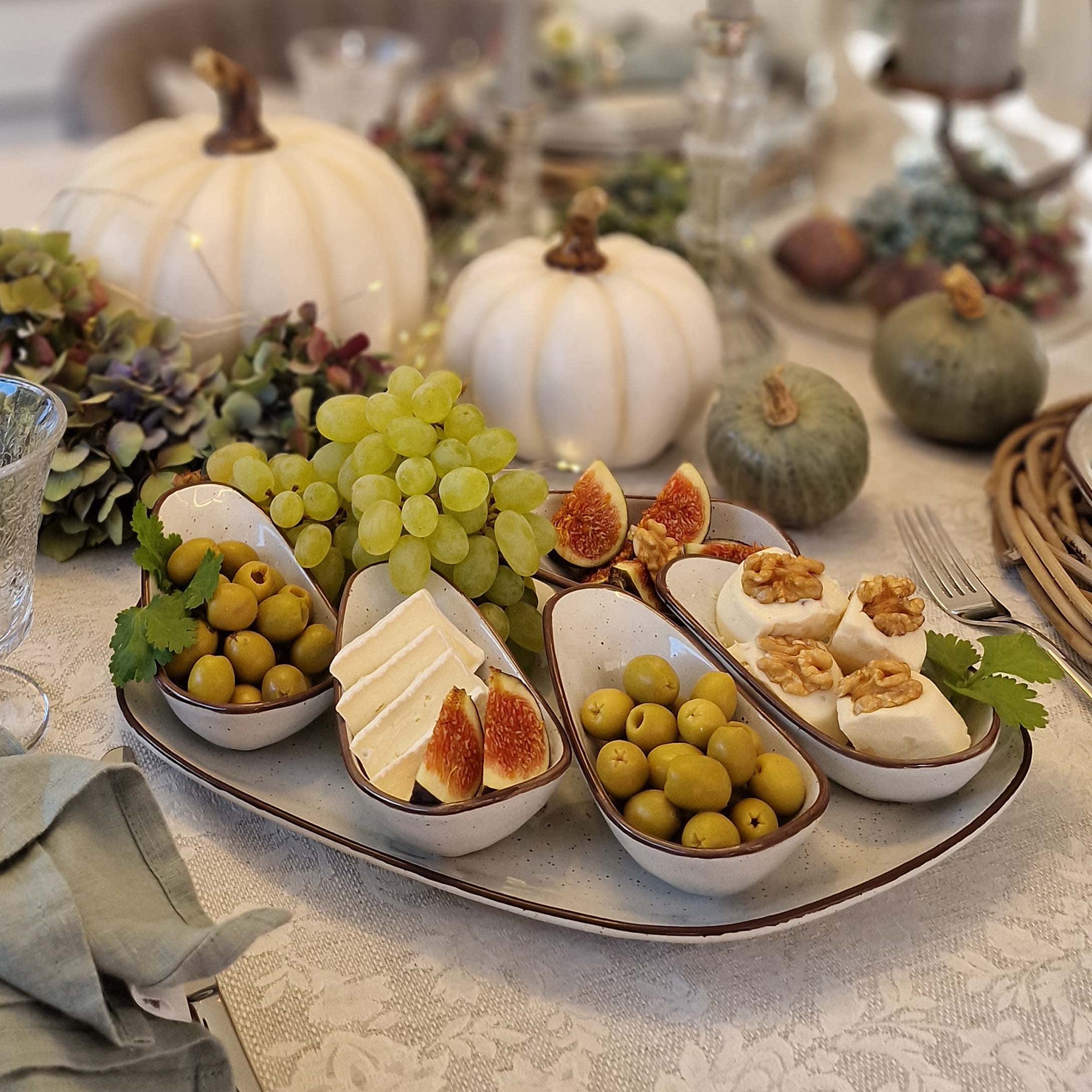 Vassoio in ceramica bianca con cinque ciotole con olive, formaggio e fichi su tavola decorata