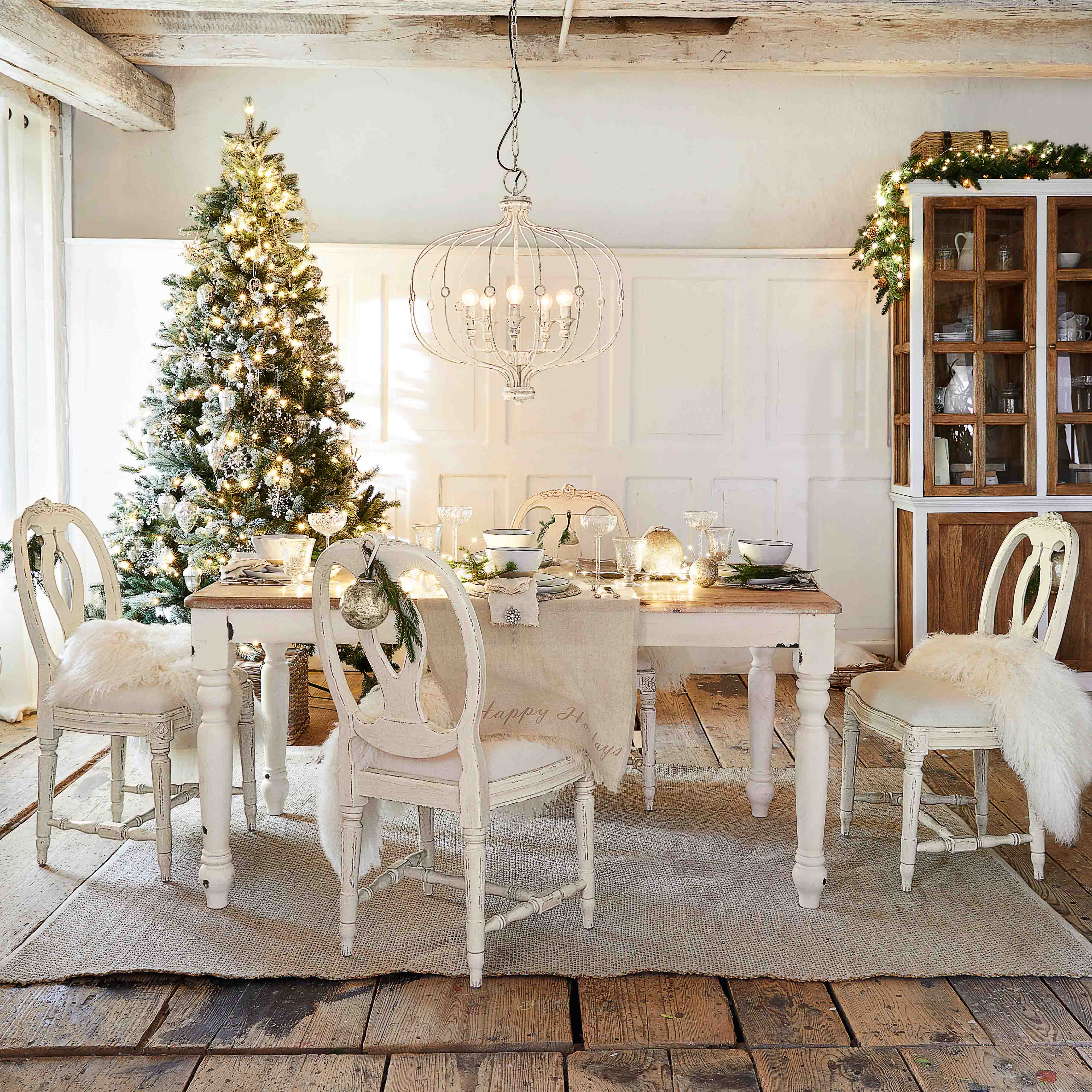 Sala da pranzo rustica con tavolo e sedie bianche in legno, decorazioni natalizie con albero e lampadario