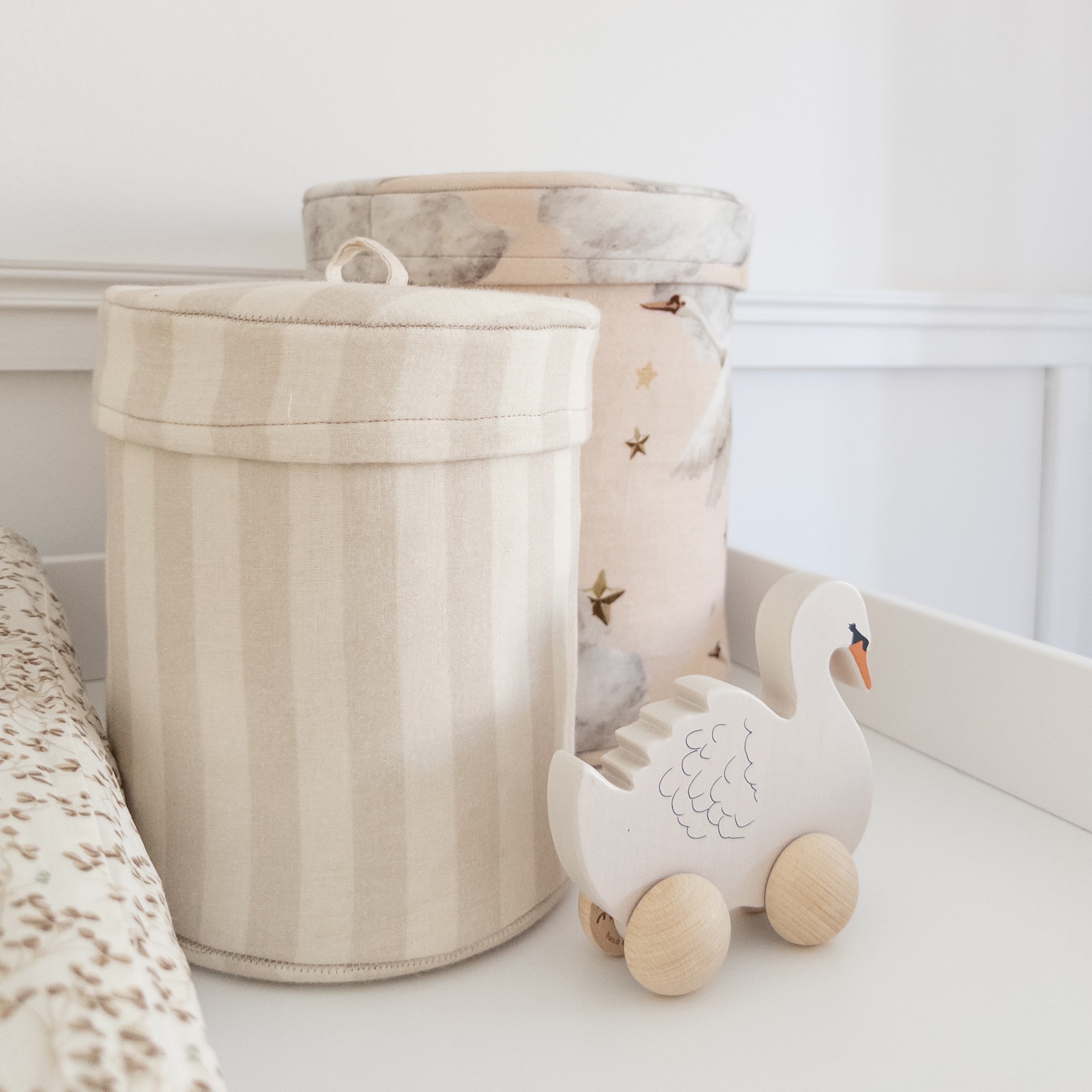 Giocattolo cigno in legno su ruote accanto a contenitori in tessuto beige in cameretta