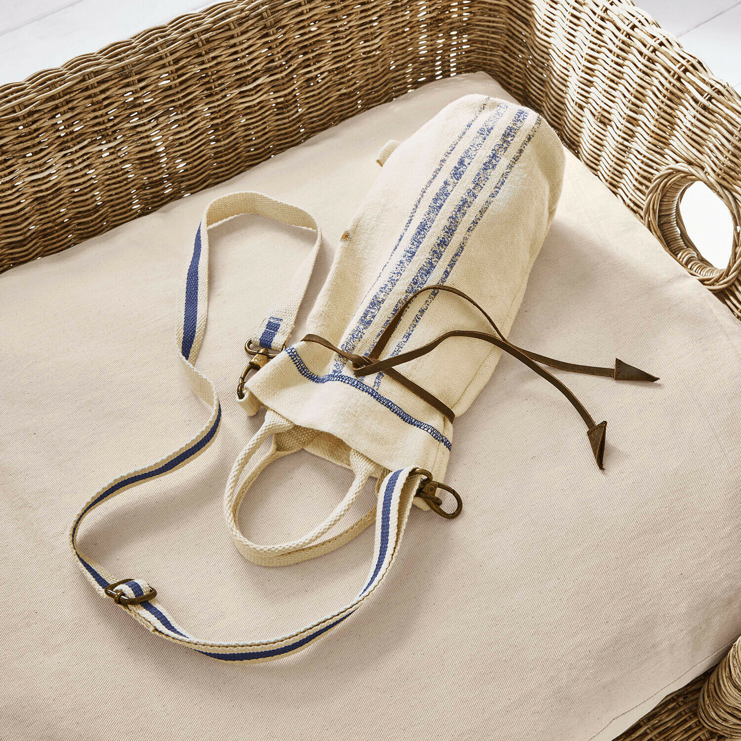 Borsetta portabottiglie Pawera Borsa in cotone beige con strisce blu e cordoncino in pelle su cuscino chiaro con schienale in vimini