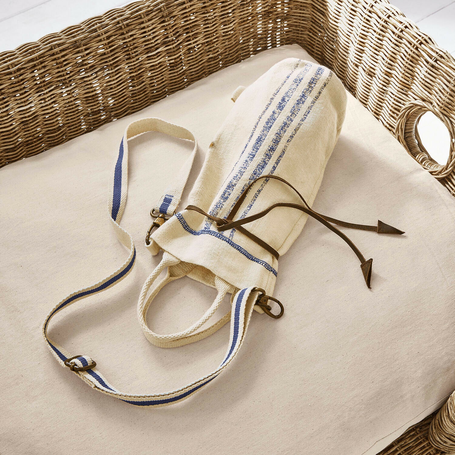 Borsetta portabottiglie Pawera Borsa in cotone beige con strisce blu e cordoncino in pelle su cuscino chiaro con schienale in vimini