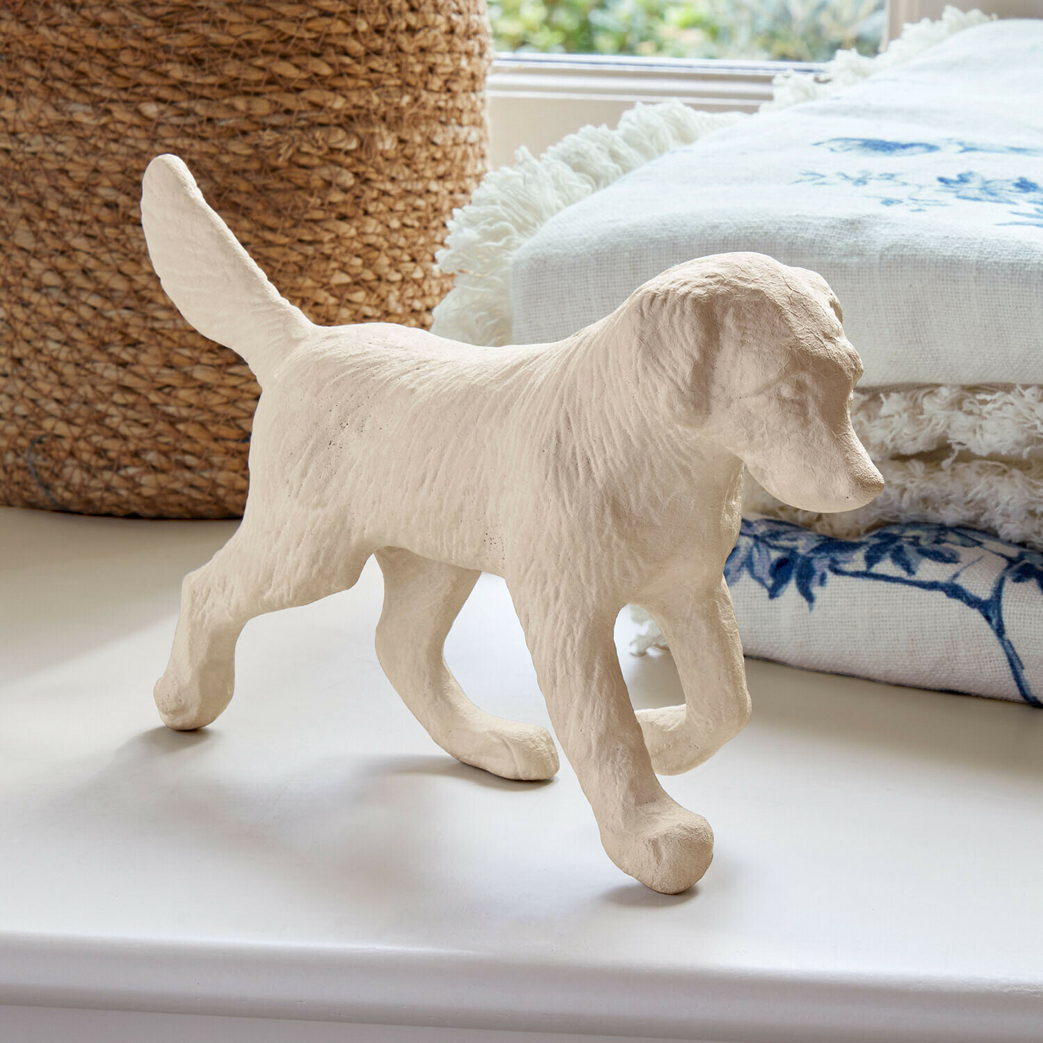 Figura di cane beige in materiale testurizzato su superficie bianca con tessuto decorativo sullo sfondo