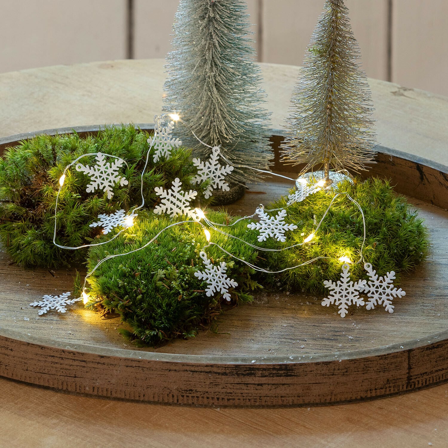 Catena luminosa a LED Azmira Ghirlanda decorativa con fiocchi di neve bianchi e luci LED su muschio verde su vassoio in legno