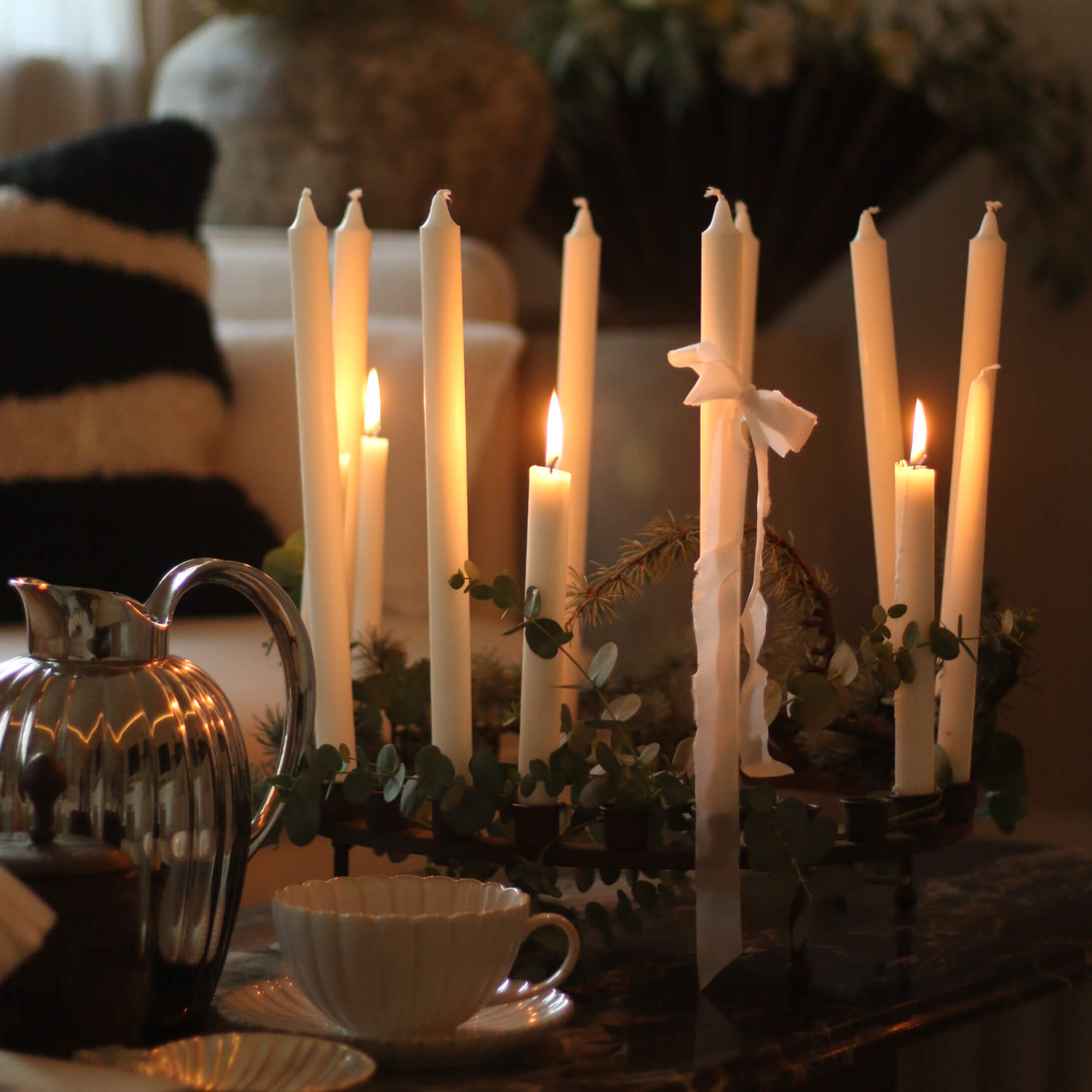 Portacandele decorativo con candele bianche e foglie verdi su tavolo in ambiente accogliente