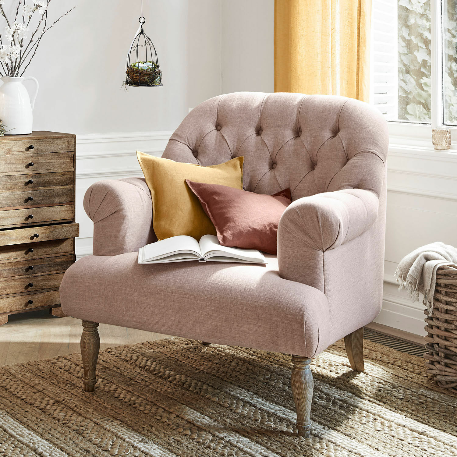 Poltrona Shambrook Divano imbottito rosa con gambe in legno e due cuscini colorati su tappeto intrecciato naturale