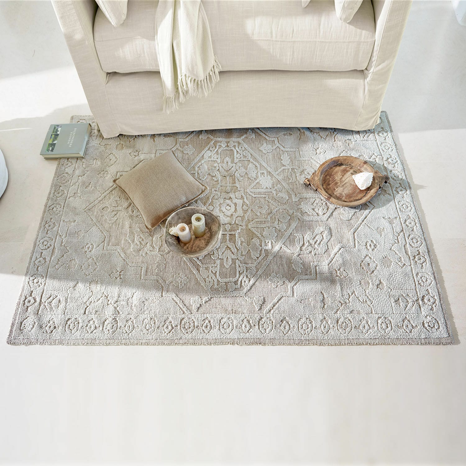 Tappeto Armidale Tappeto beige con motivo delicato sotto un divano chiaro, cuscino e decorazioni sul pavimento