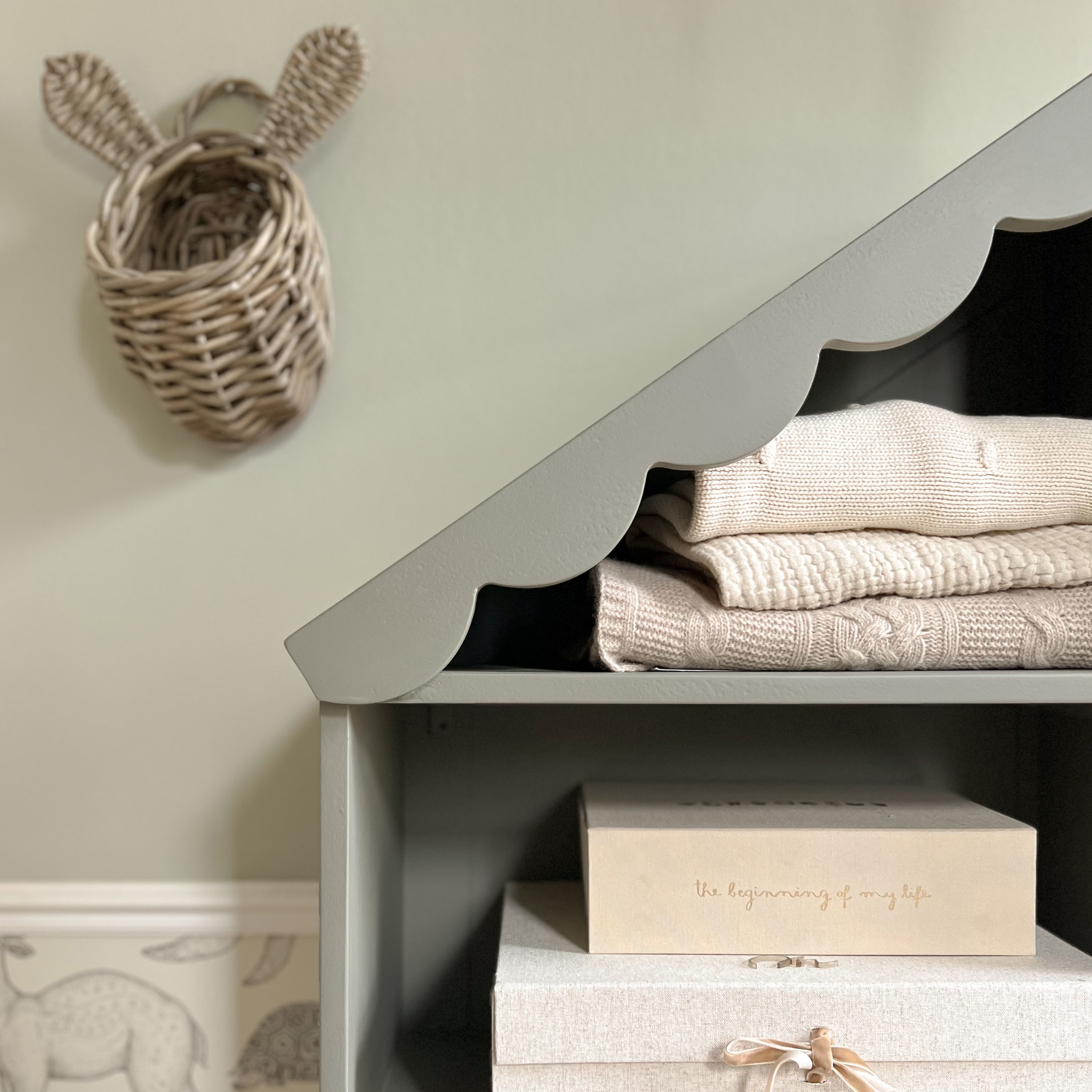 Mensola grigia in legno con bordo ondulato, maglioni beige piegati e scatole decorative