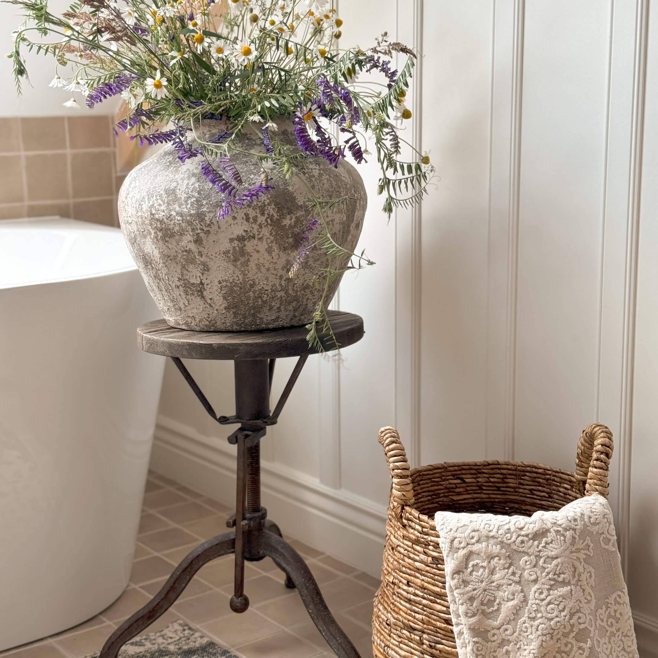 Vaso rustico in pietra grigia con fiori di campo su supporto metallico in bagno