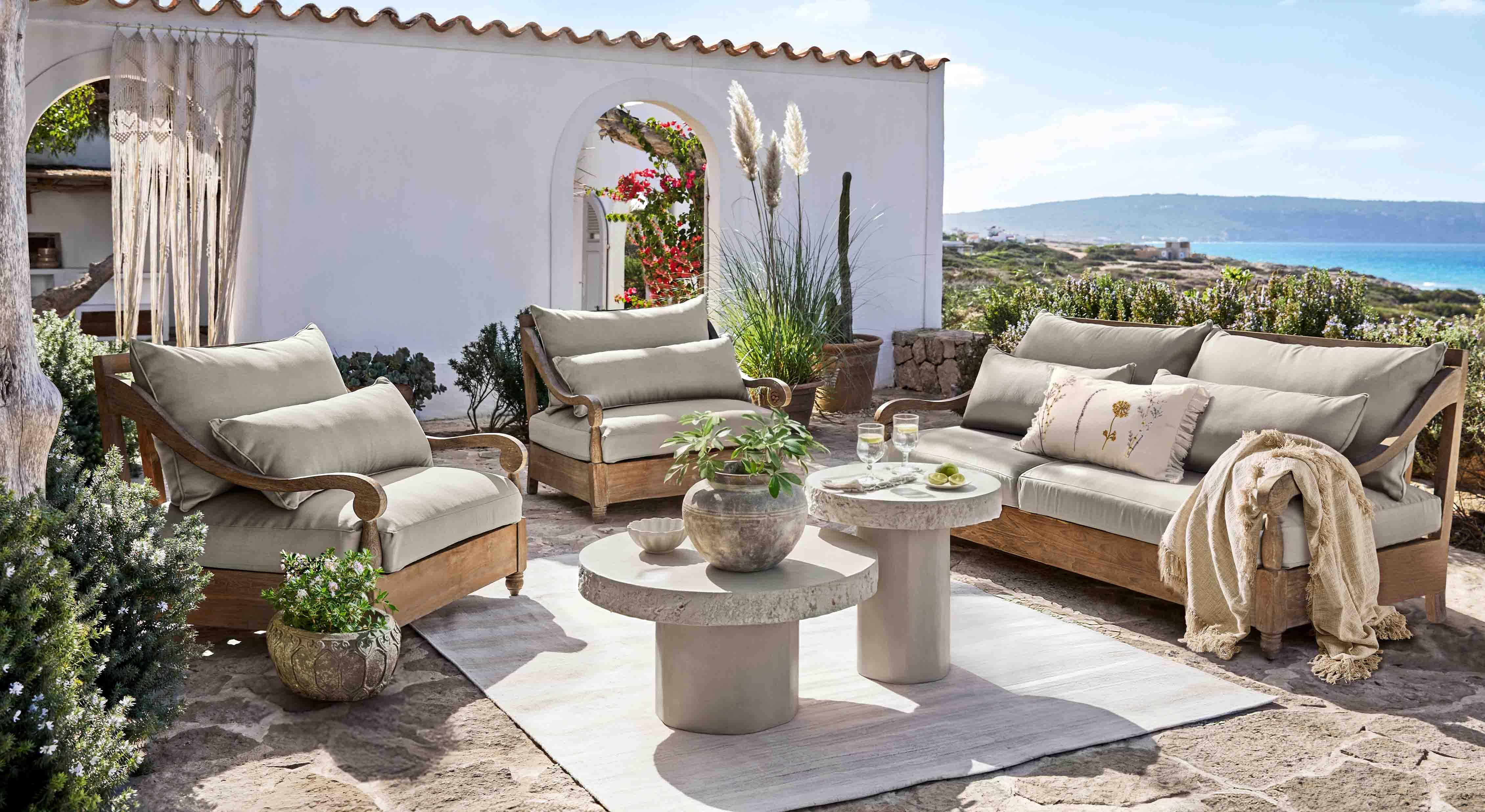 Set di mobili da giardino in legno con cuscini grigi su terrazza con vista mare