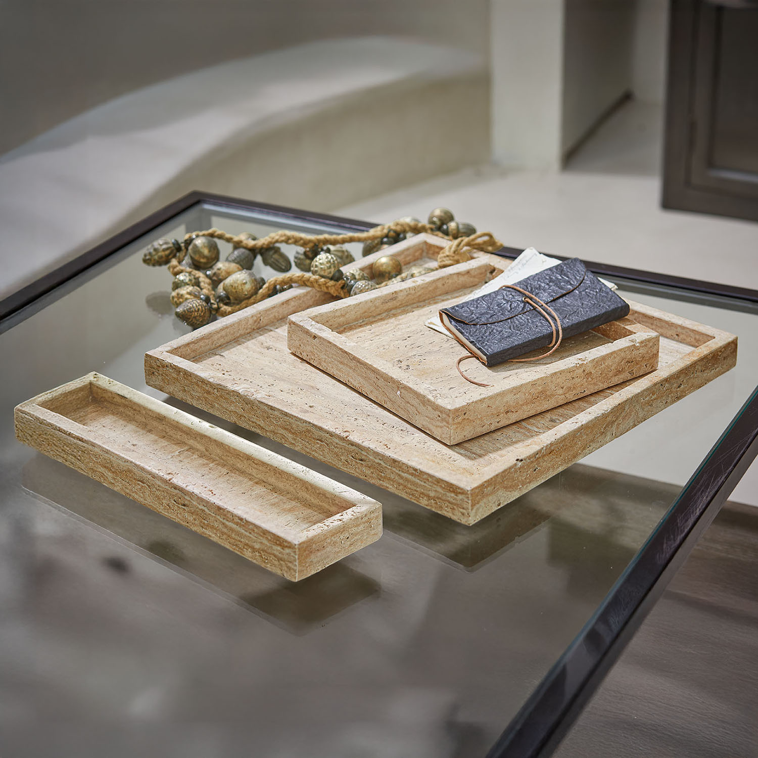 Set di tre vassoi rettangolari in pietra beige su tavolo in vetro con cornice nera