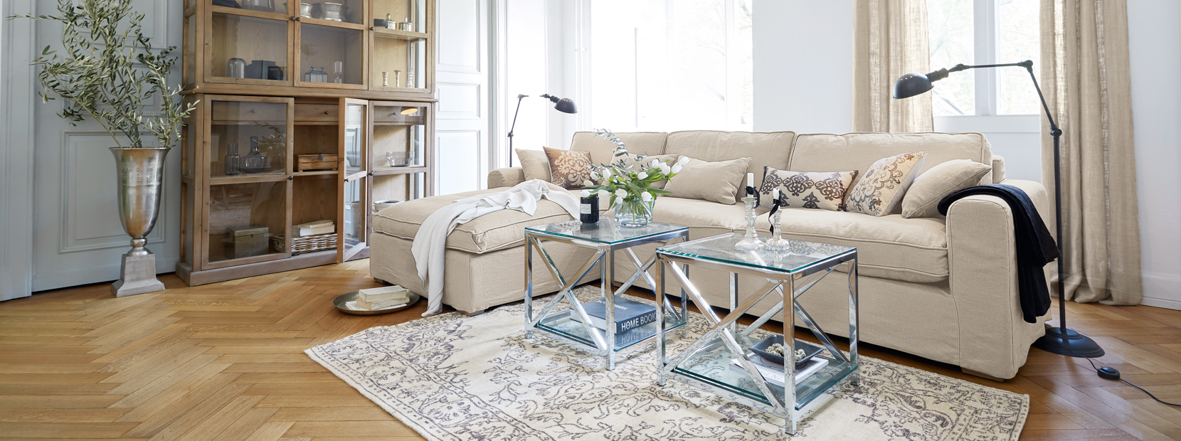 Soggiorno classico elegante con divano beige, tavolini in vetro e vetrina in legno su pavimento chiaro