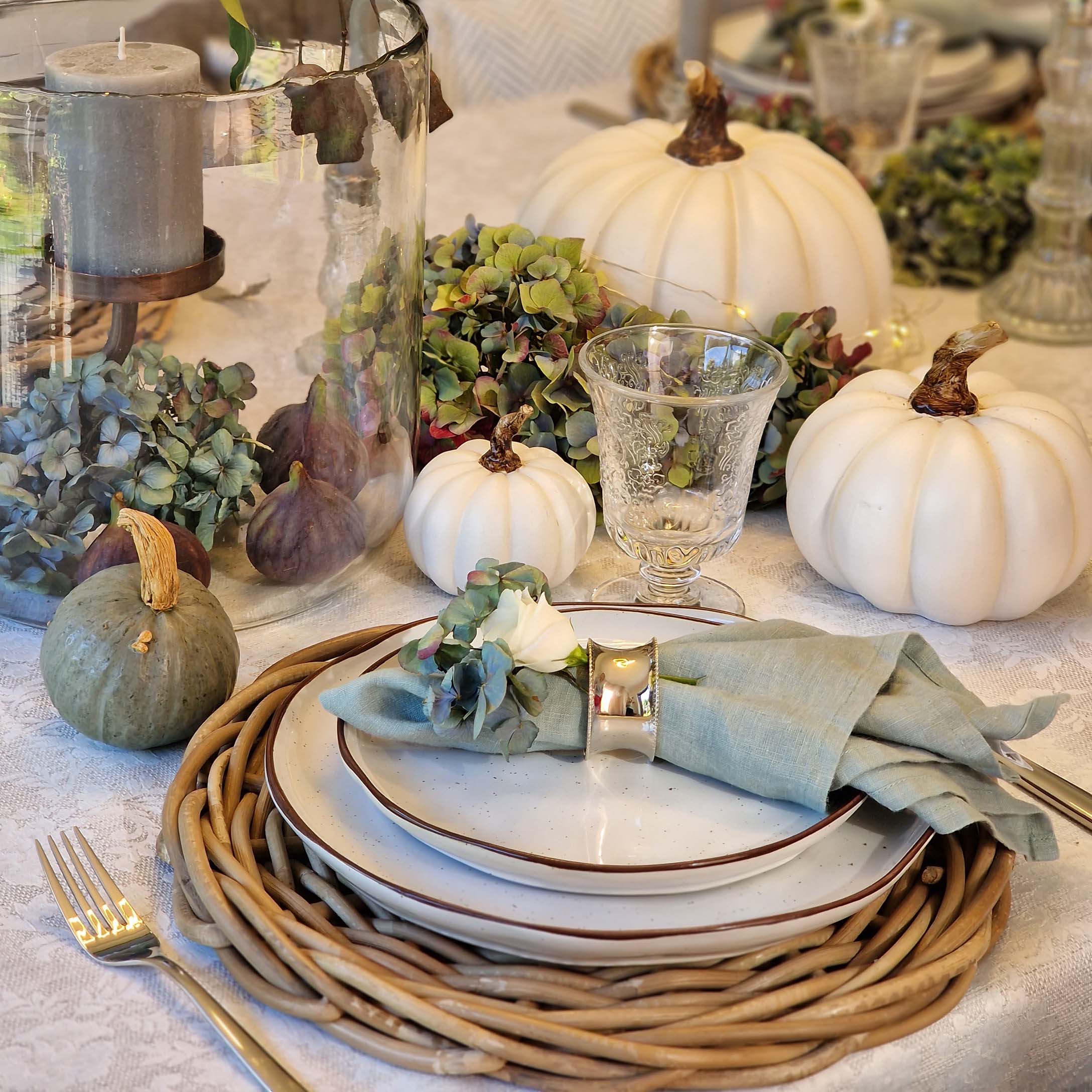 Decorazione da tavola con zucche bianche e verdi, bicchiere e tovagliolo di lino su piatti in ceramica